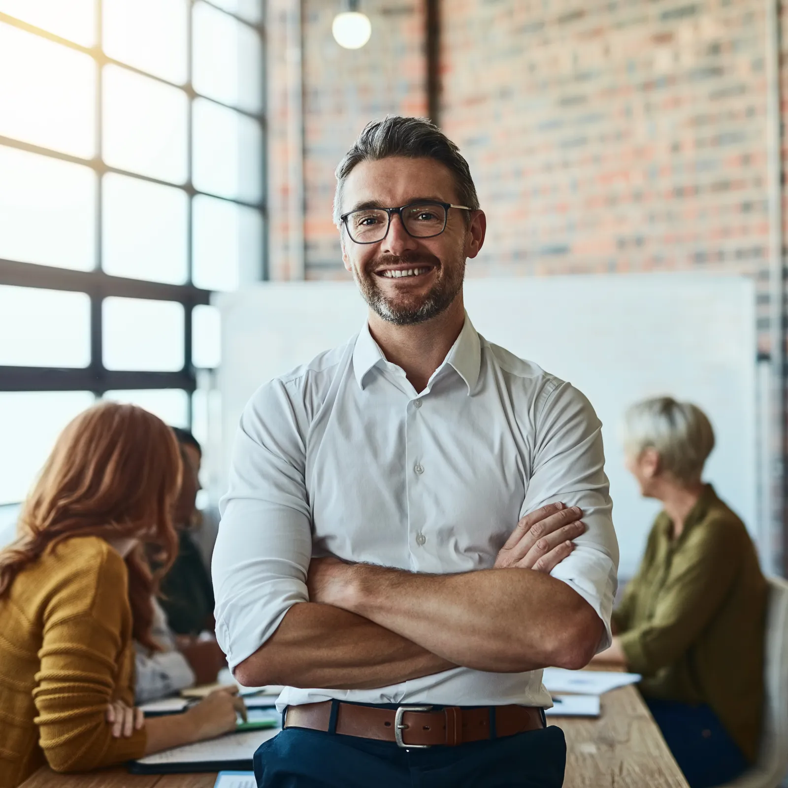 Smiling businessman stands confidently in a modern office during a team meeting.