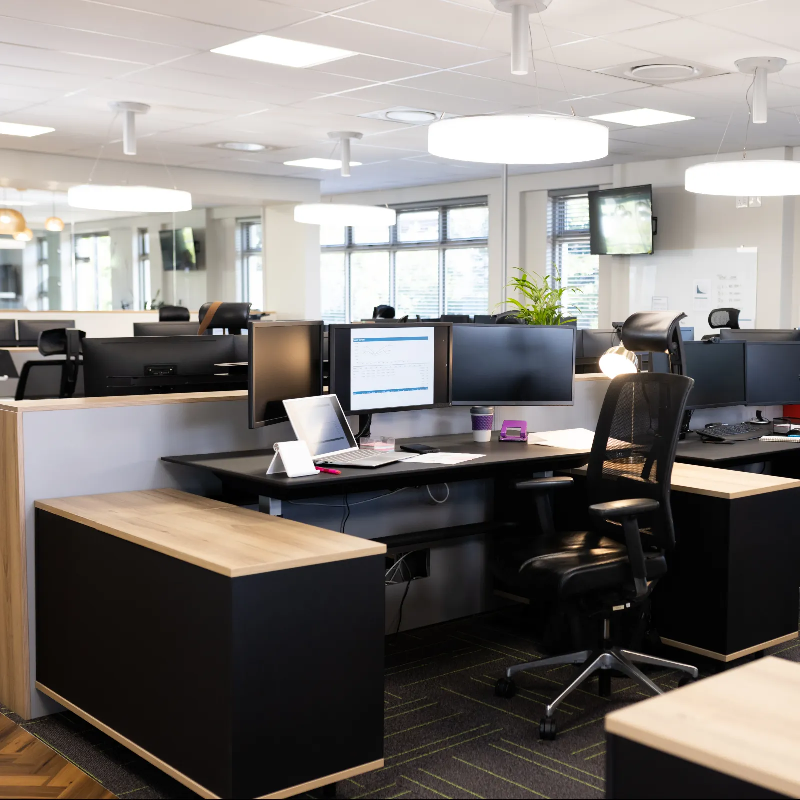 Modern office workspace with desks, ergonomic chairs, and contemporary lighting.