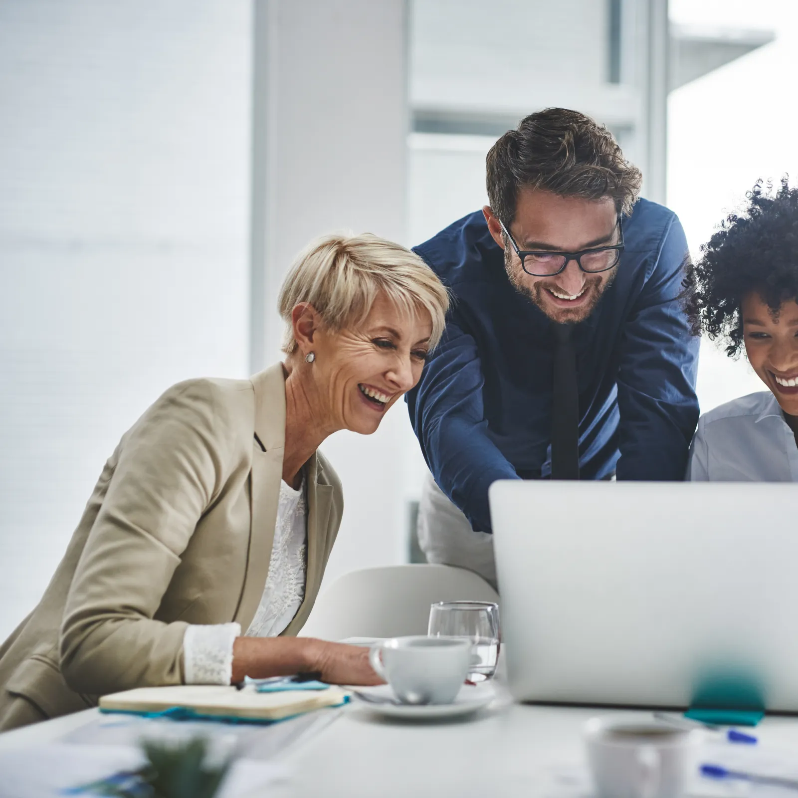 Three professionals collaborating on a laptop in a bright office environment.