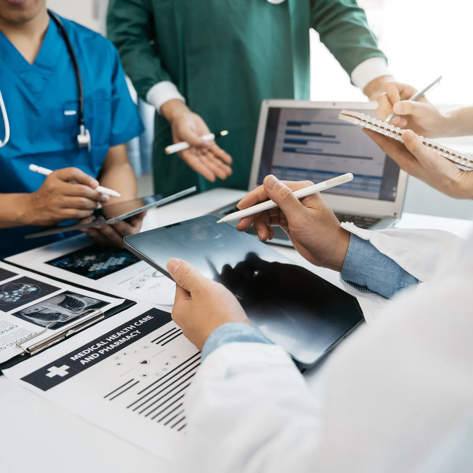 Medical professionals discussing patient data using tablets and charts in a clinical setting.