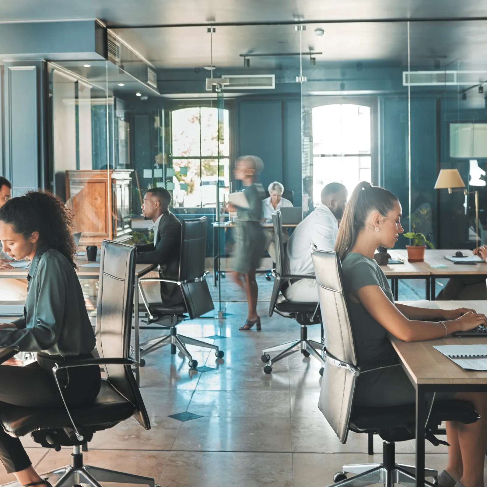 Modern office environment with people working at desks and collaborating in a bright, open space.