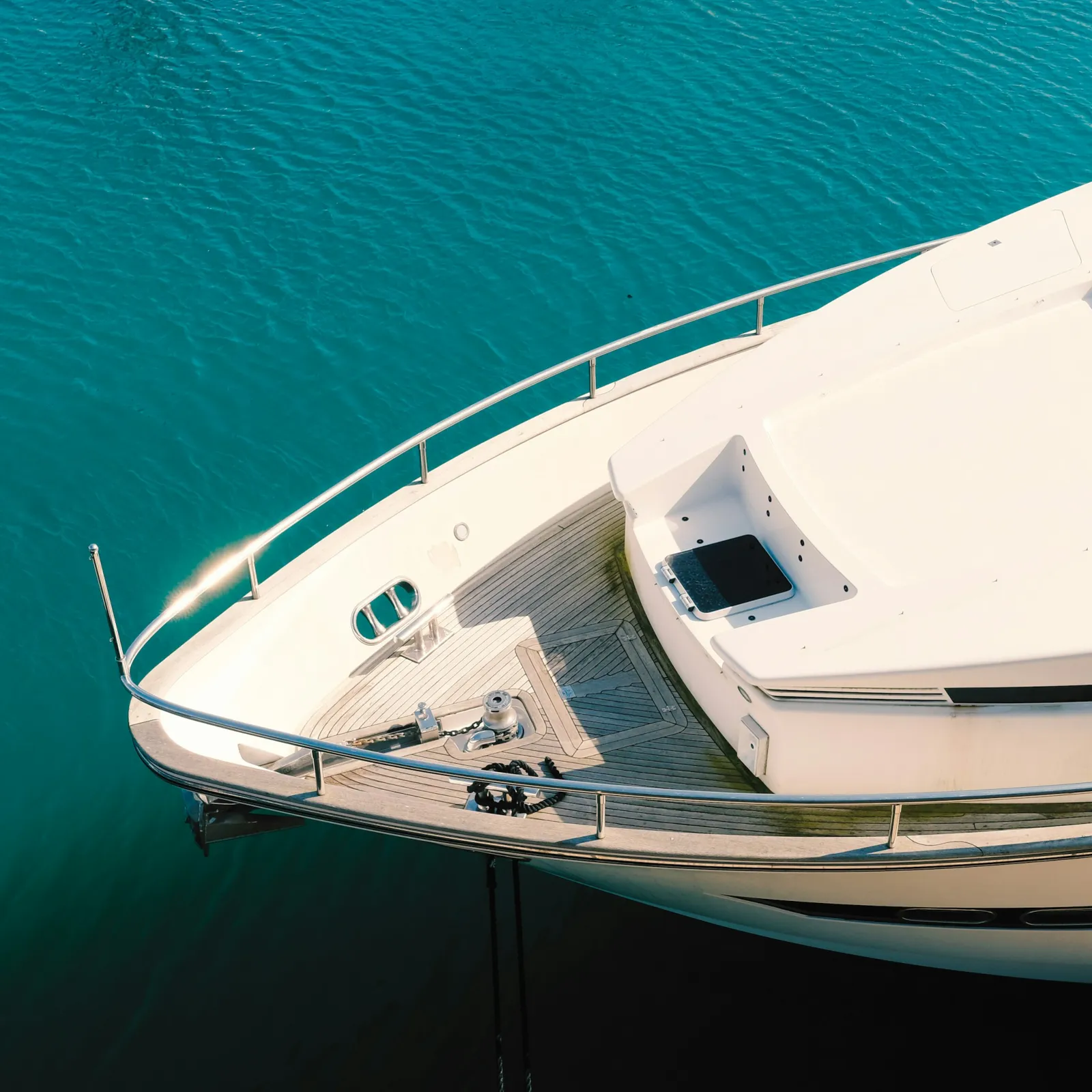 Bow of a white yacht floating on calm turquoise water under bright sunlight