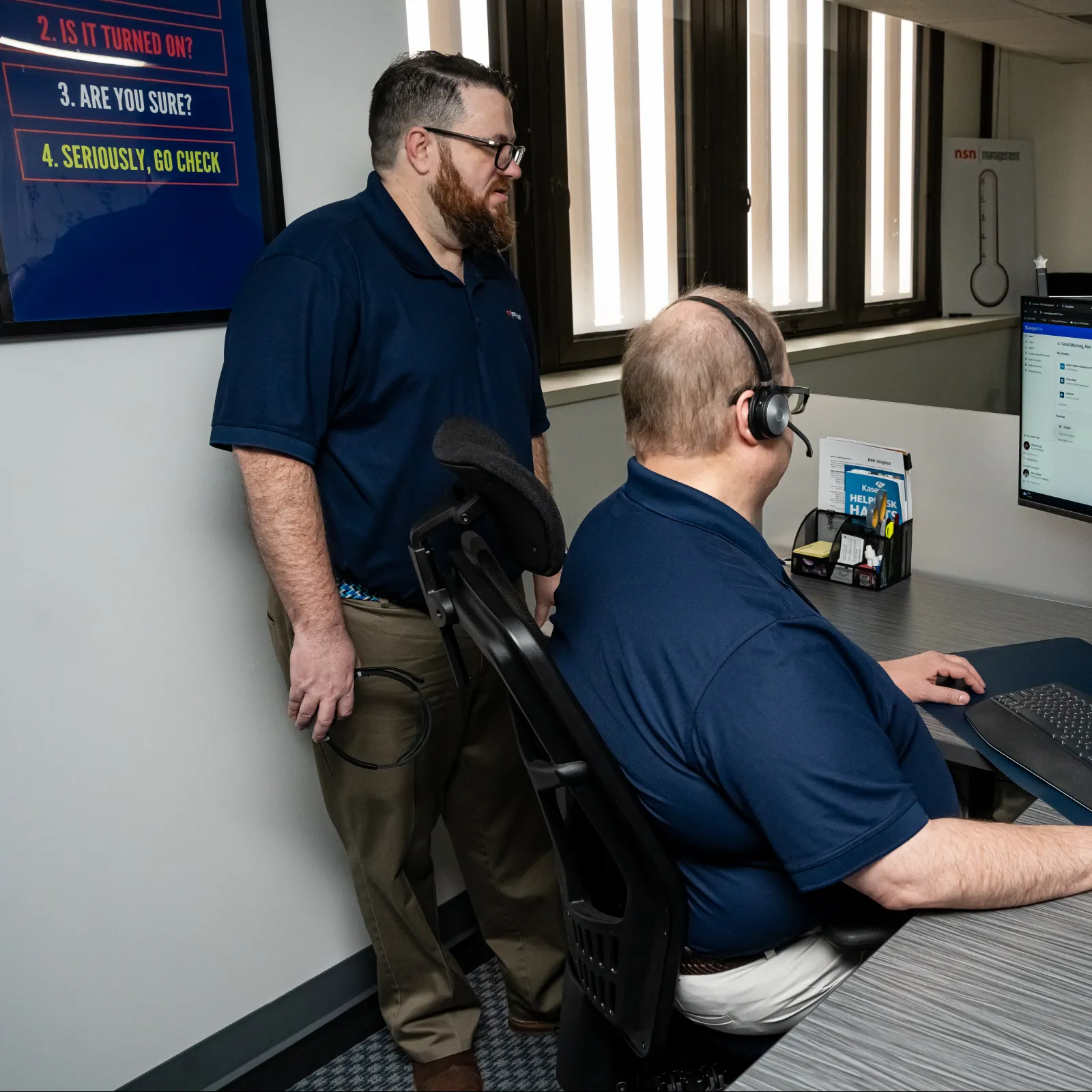 a man sitting at a desk with a man standing next to him