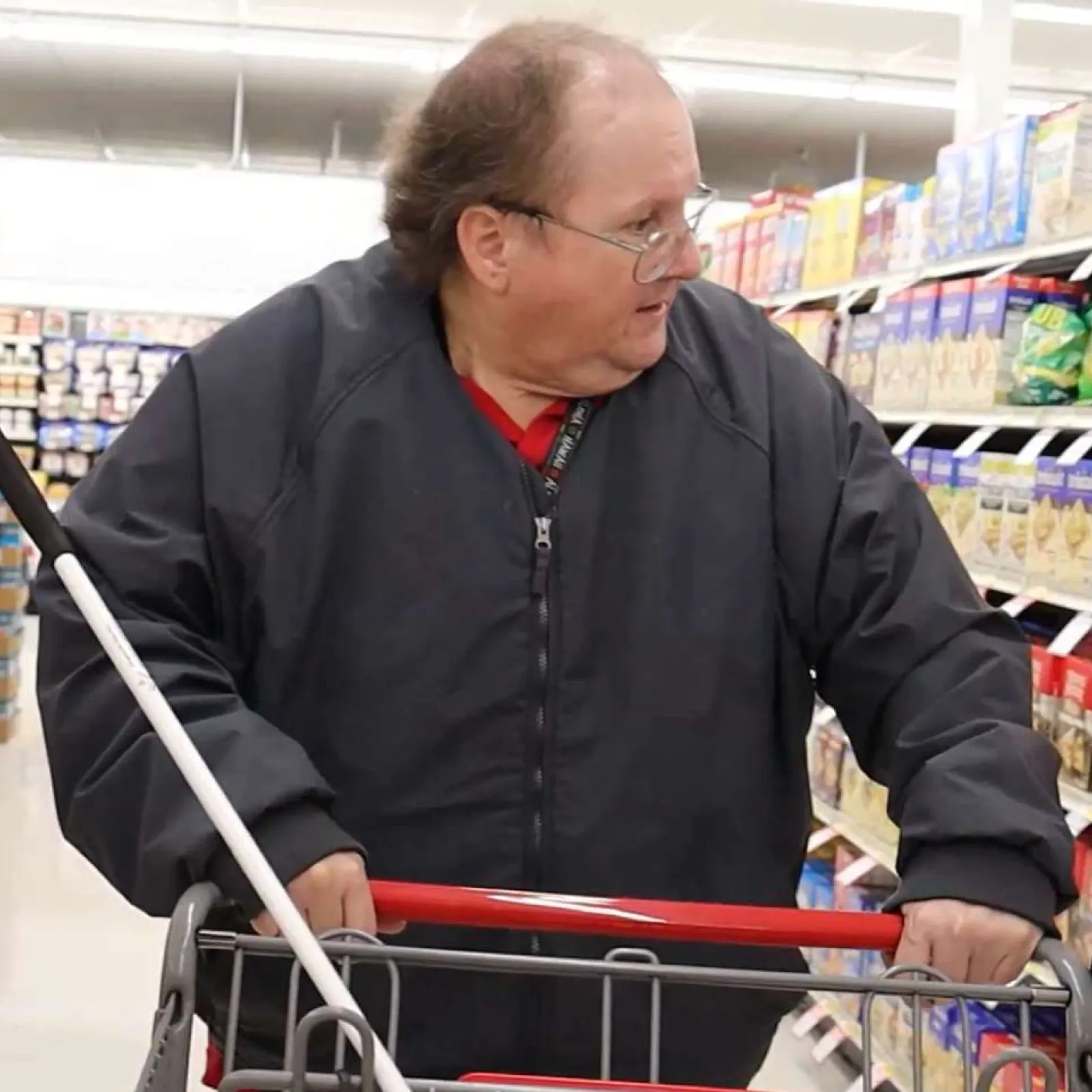 Man with white cane shopping in grocery store aisle filled with snacks and condiments.