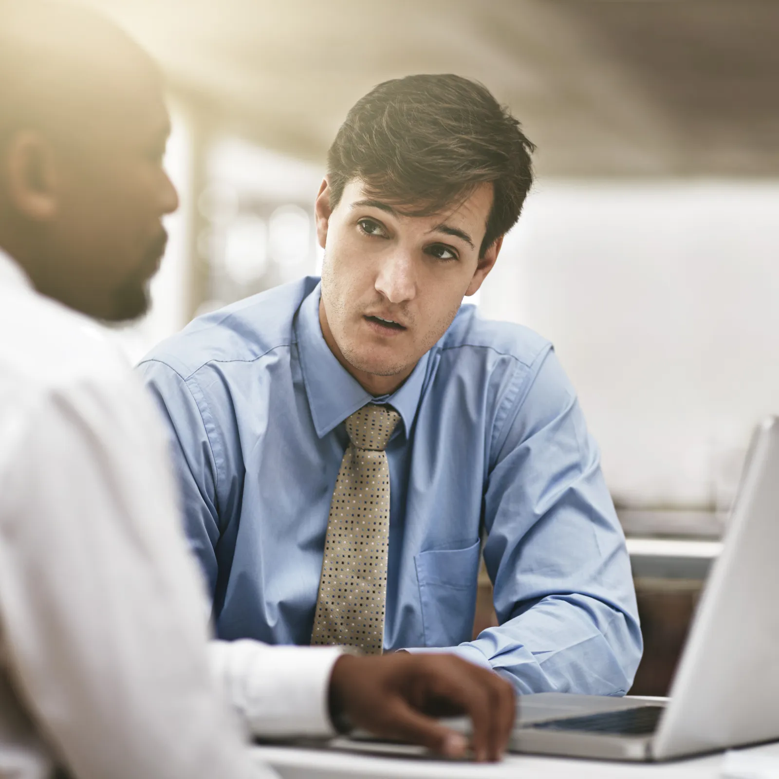 Two businessmen in a discussion with a laptop on the table in a bright office setting.