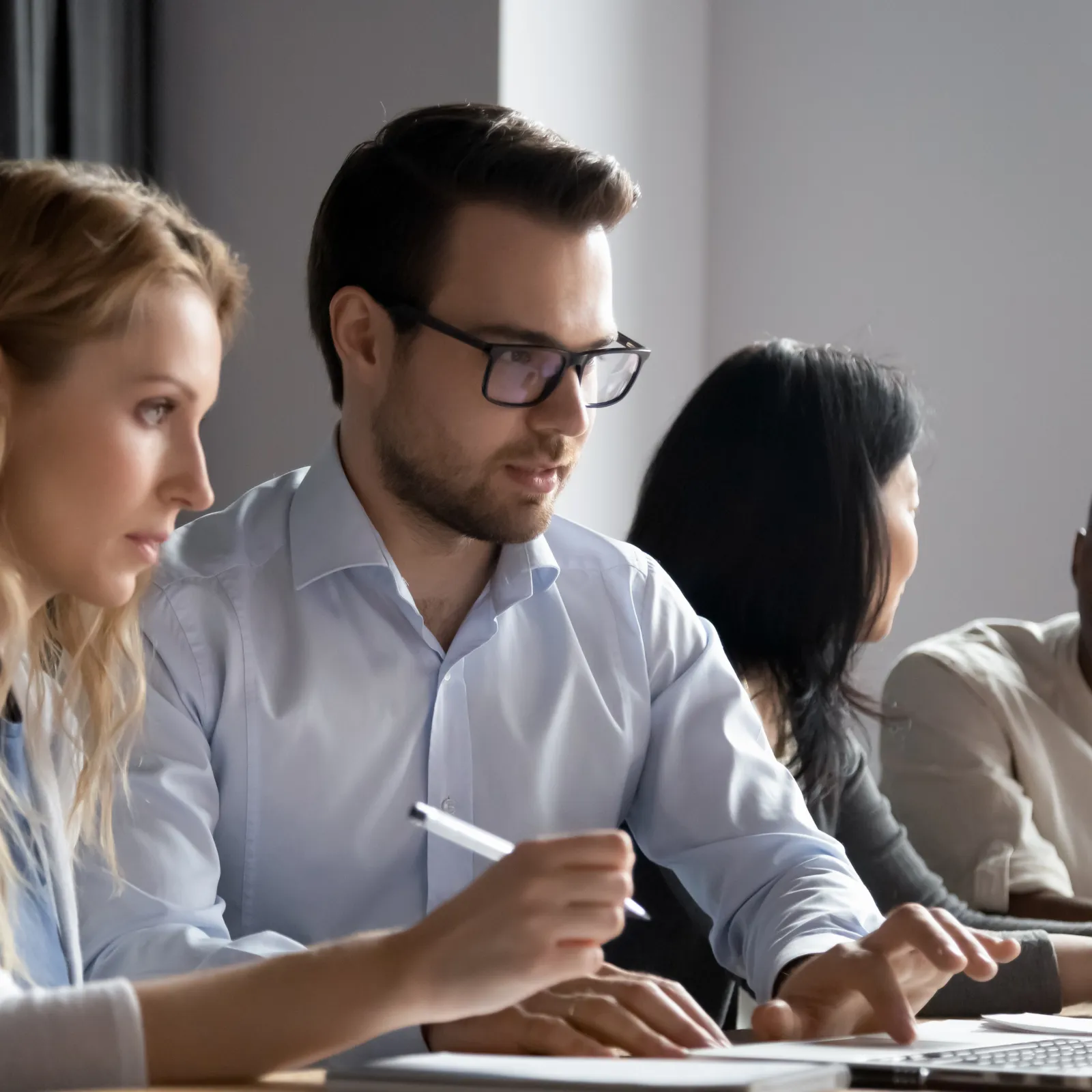 Four diverse coworkers collaborating on a project using a laptop in a bright office environment.