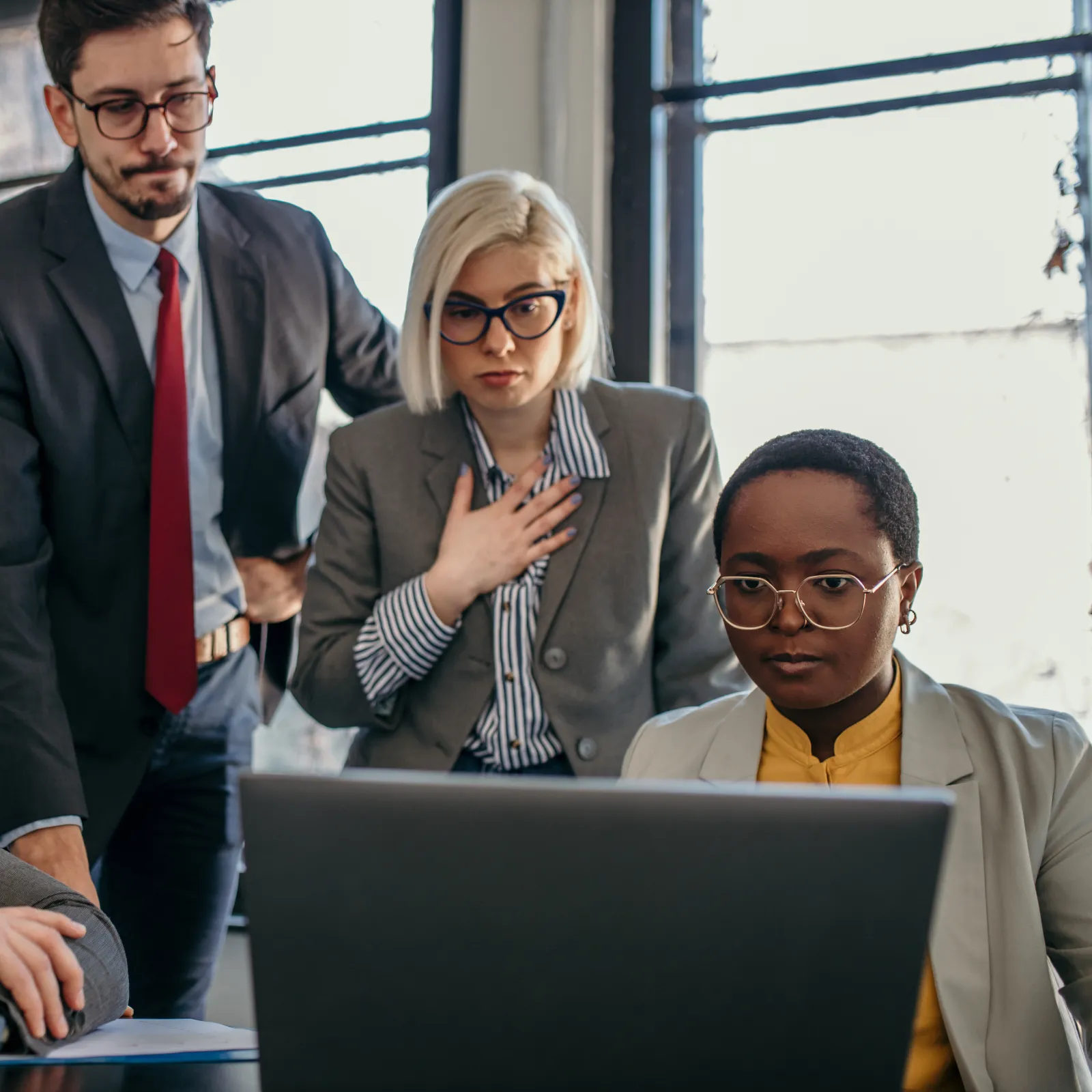 Diverse business team in formal attire focused on laptop screen during office meeting.