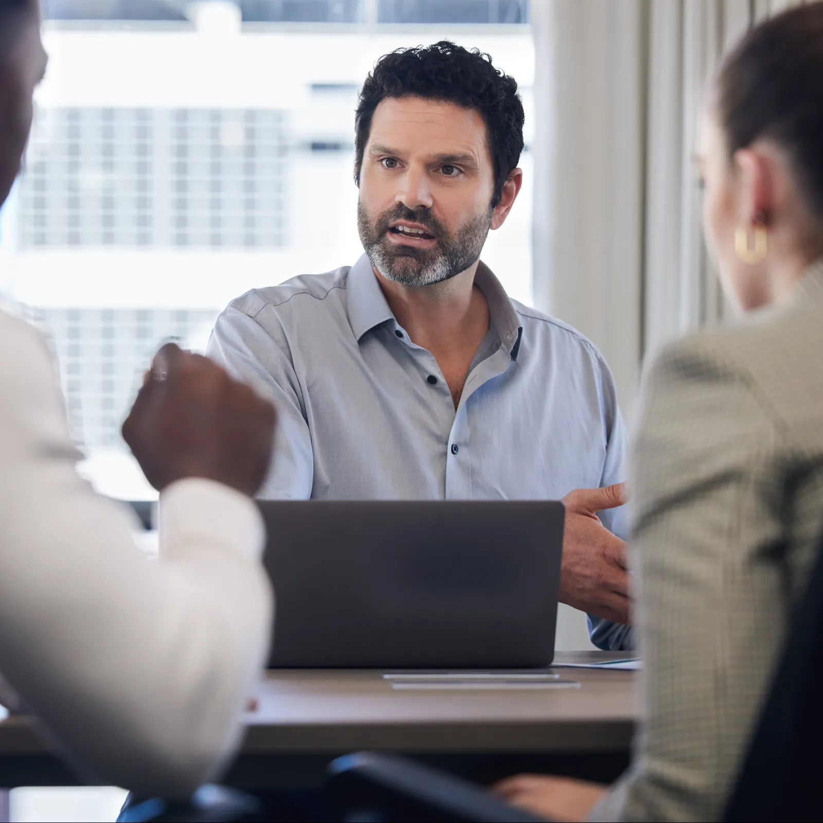 Business meeting with a man explaining ideas to colleagues around a table with a laptop in a bright office.