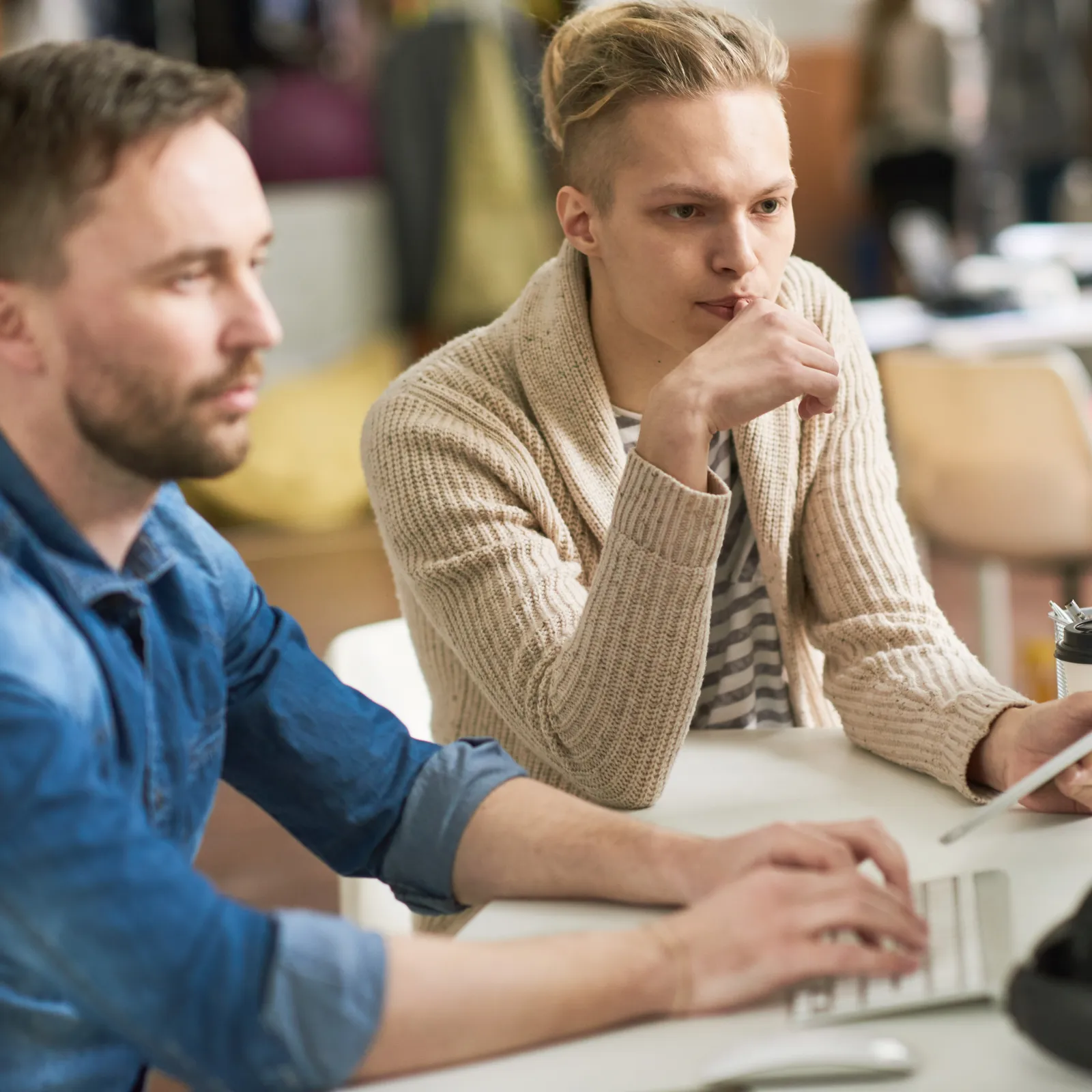 Two men focused on coding displayed on a desktop screen in a modern office workspace.