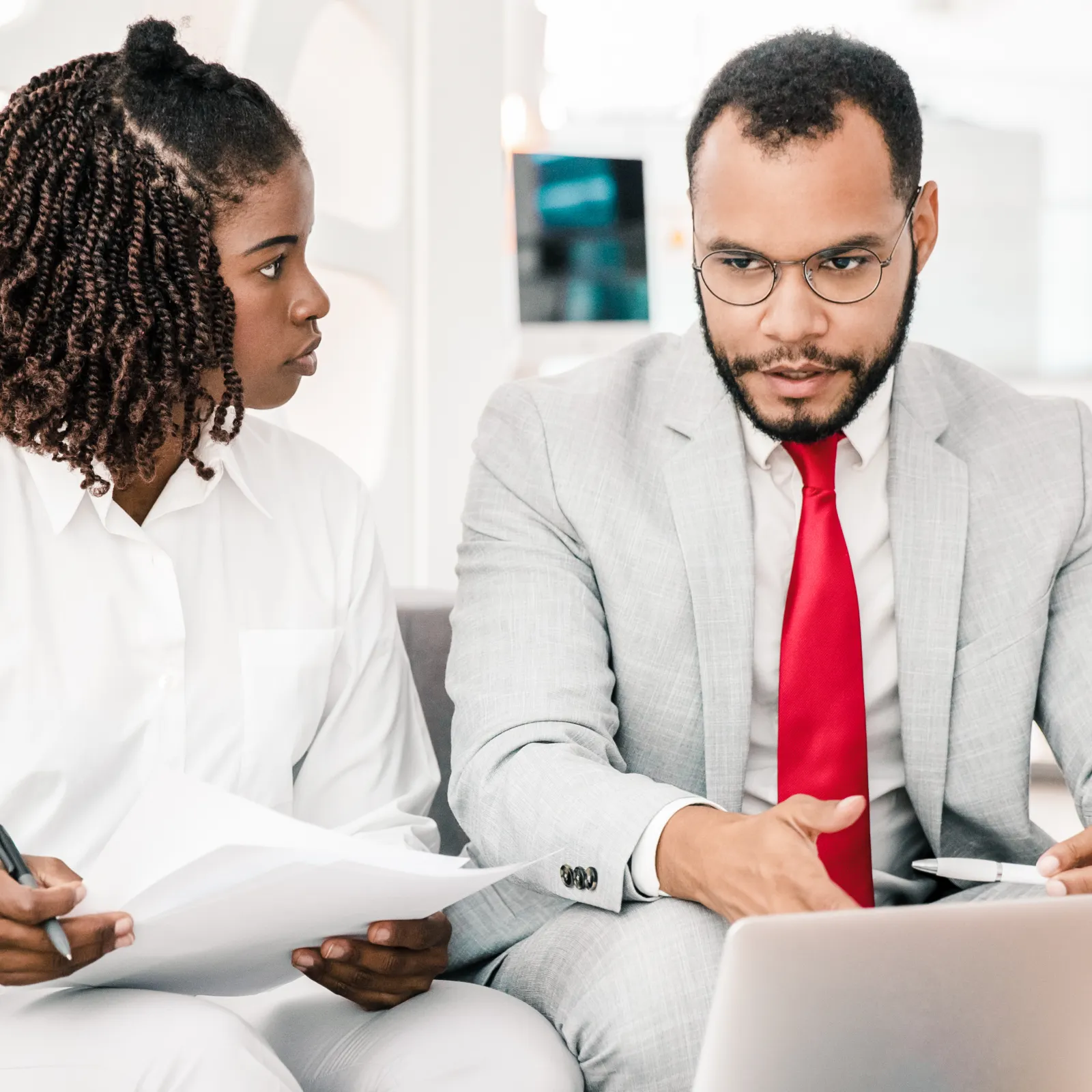 Business professionals in formal attire discussing documents and laptop during a meeting in modern office.