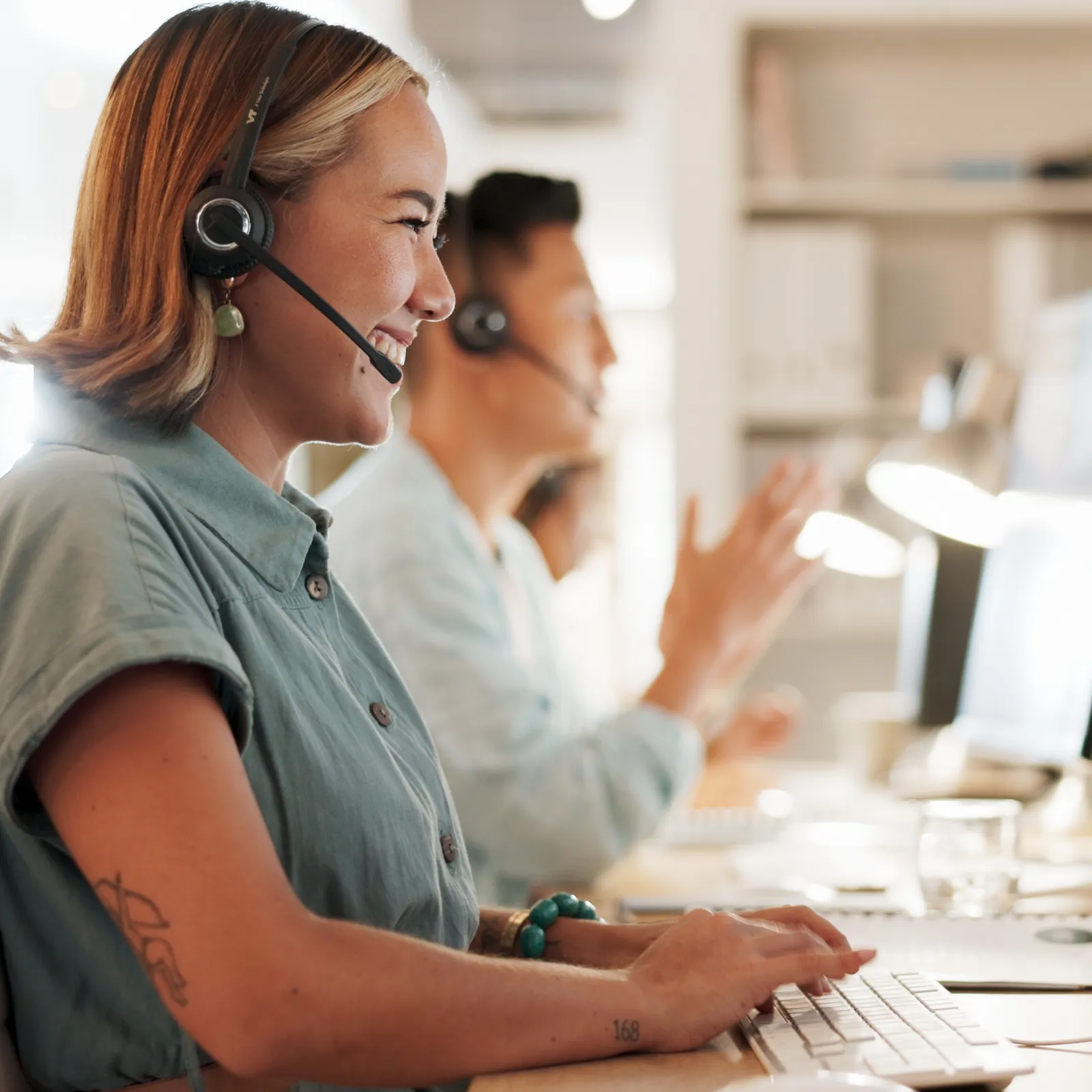 Smiling customer service representatives wearing headsets and working on computers in modern office.