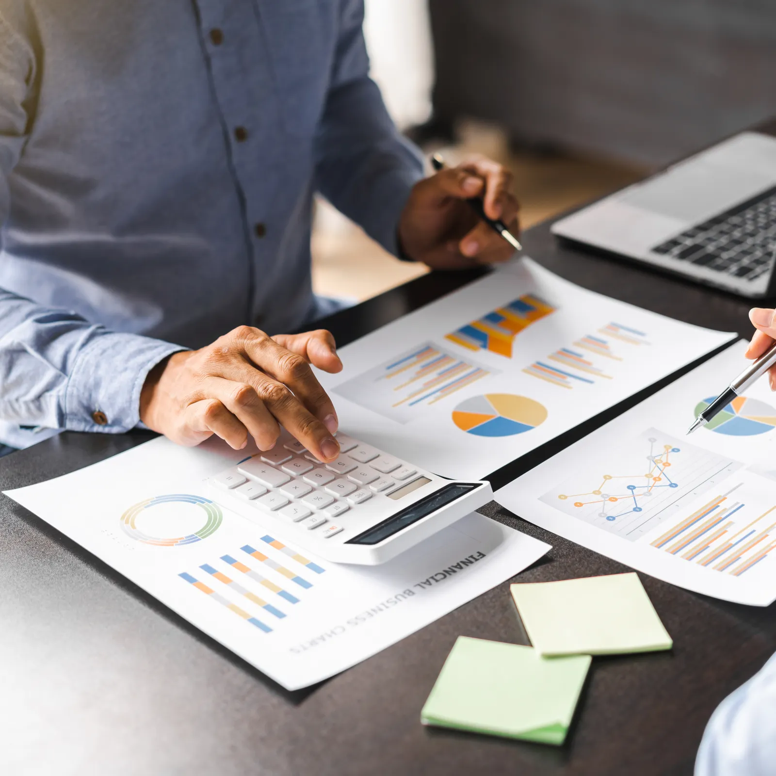 Two professionals analyzing financial charts and data with a calculator and laptop at a desk.