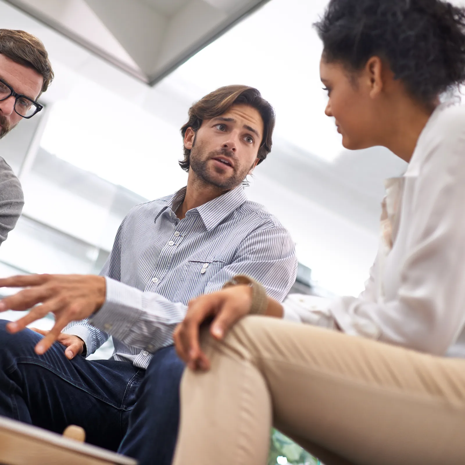 Three colleagues engaged in a discussion around a laptop in a modern office setting with natural light.
