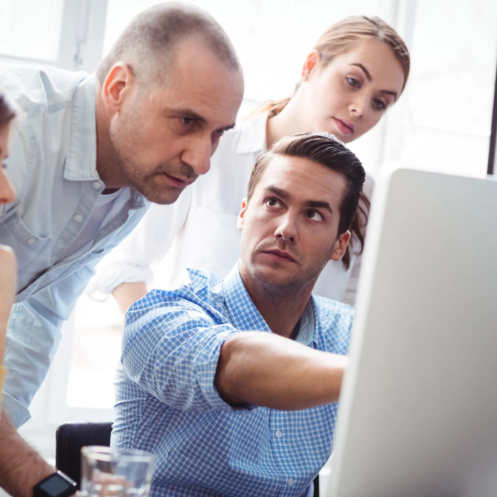 Four colleagues collaborating and discussing a project while looking at a computer screen in a bright office.