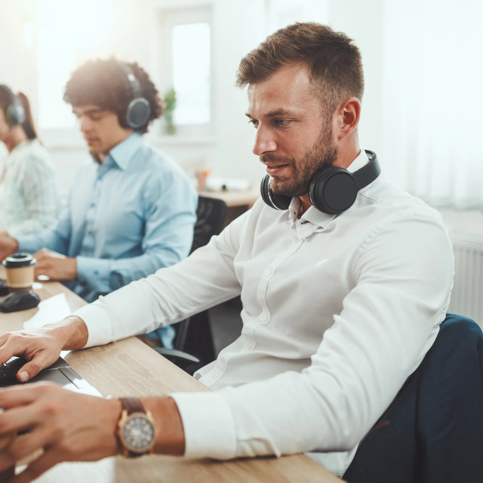 Three young professionals working on laptops with headphones in a bright modern office setting