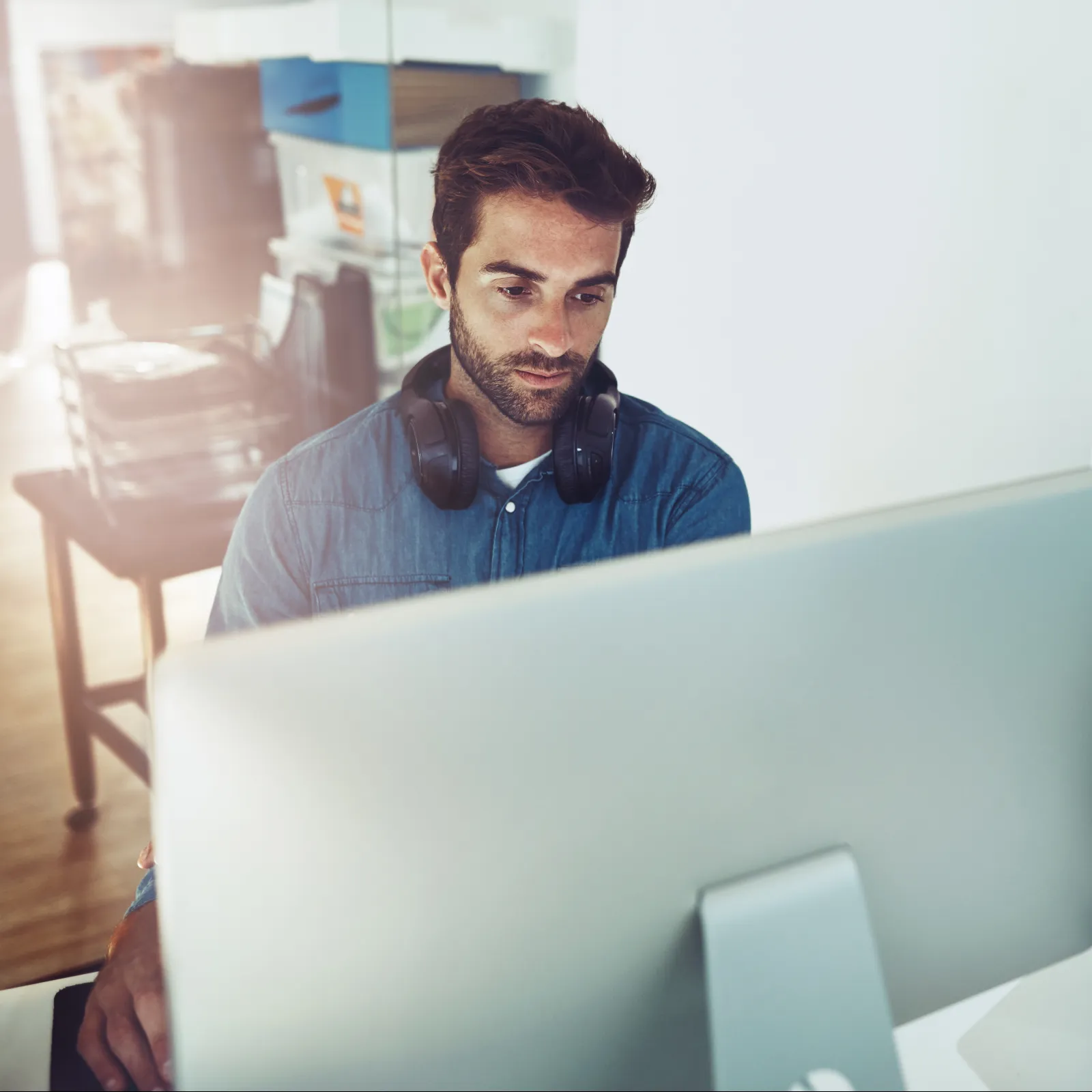 Man with headphones working at a computer desk in a modern office space with natural light.