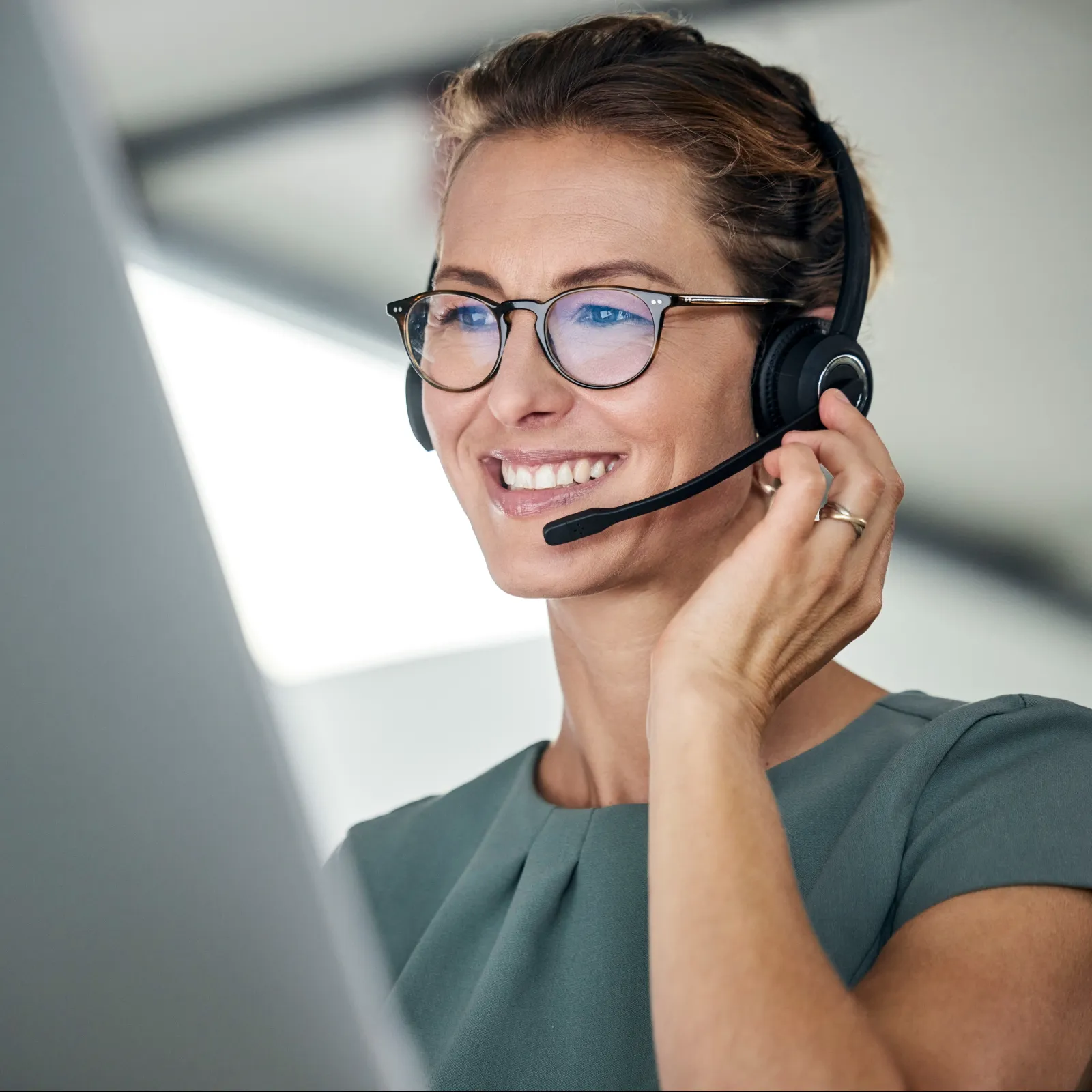 Smiling woman wearing glasses and headset working on a computer in a bright modern office space