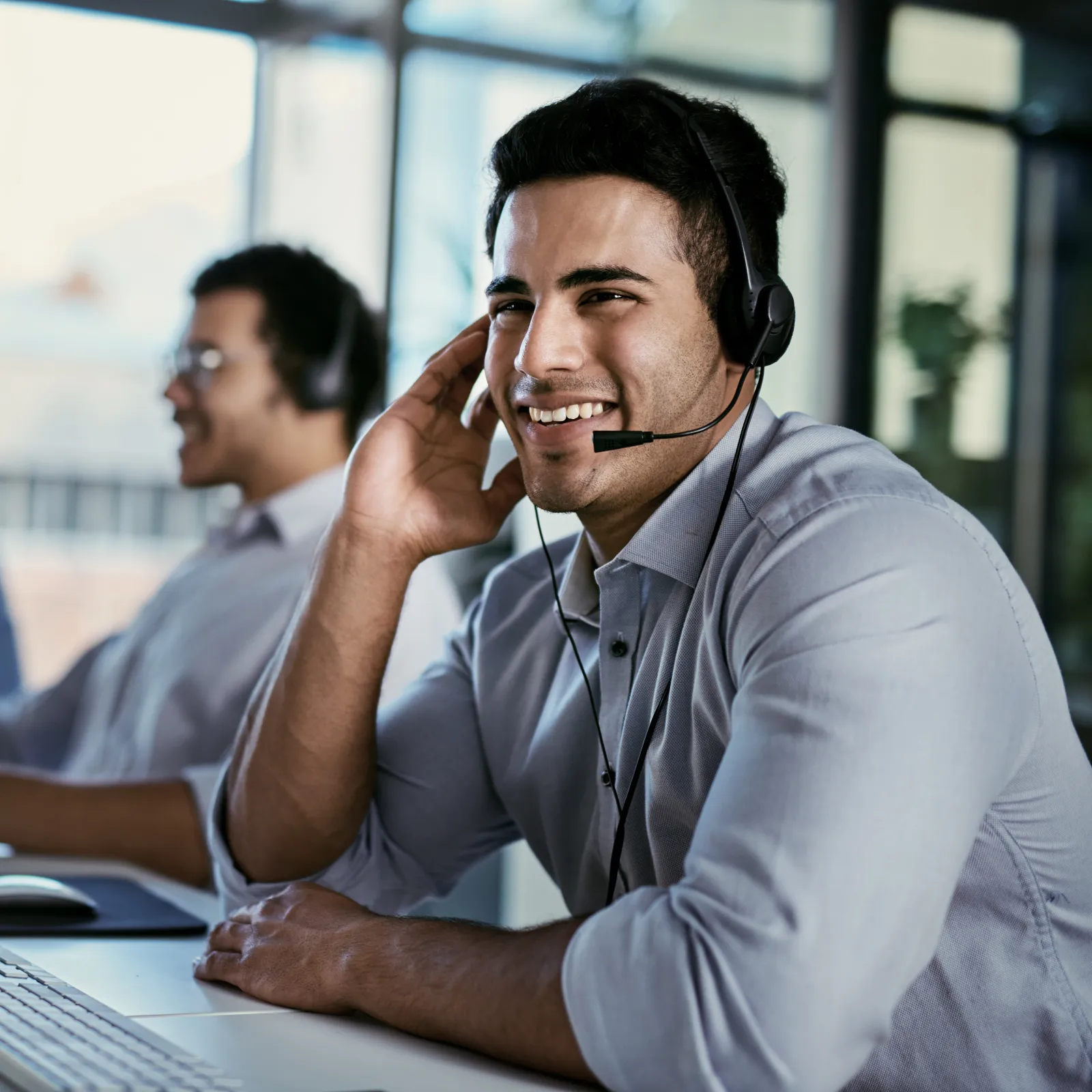 Smiling customer service representatives wearing headsets working at computers in a bright office environment