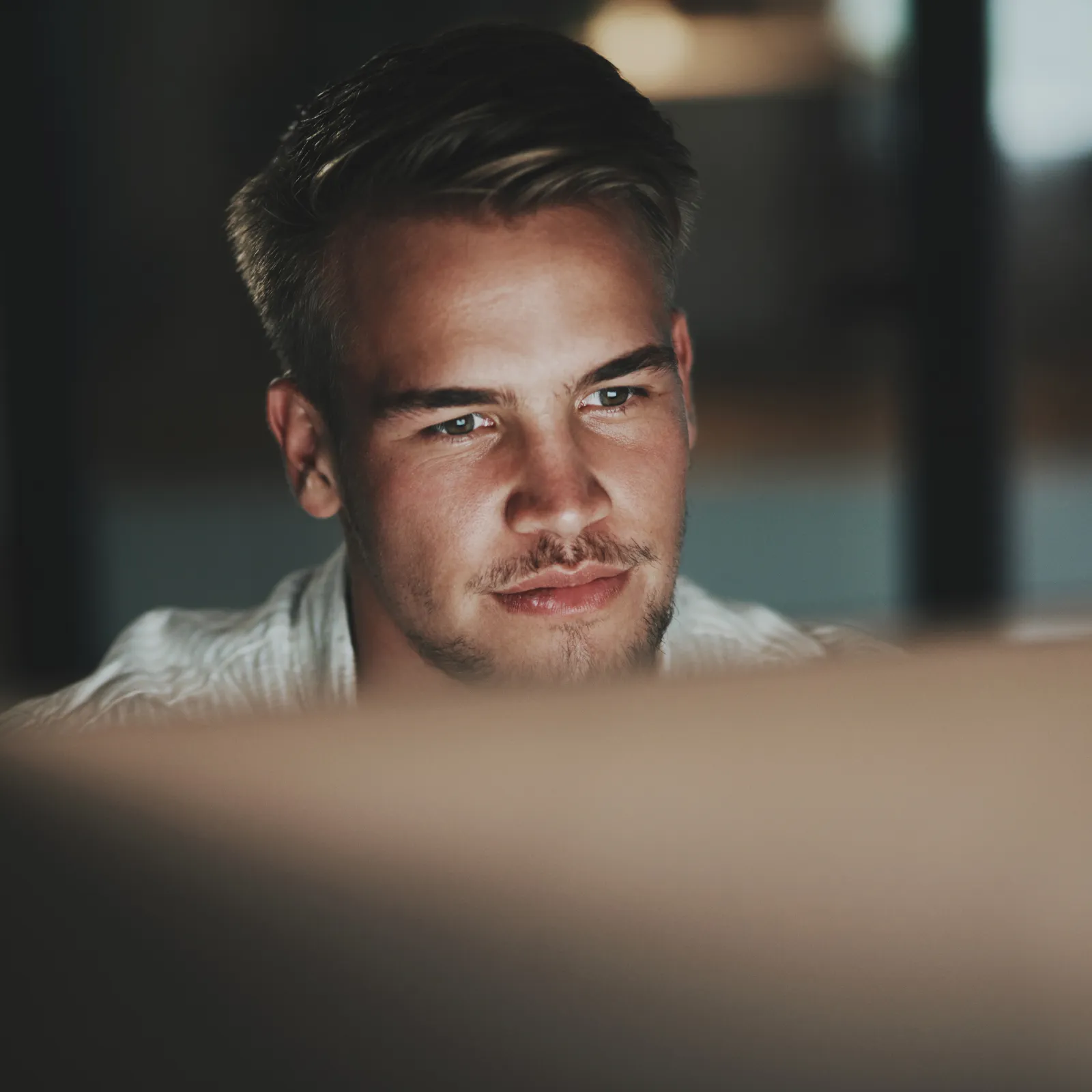 Young man focused on computer screen in a dimly lit room working late at night