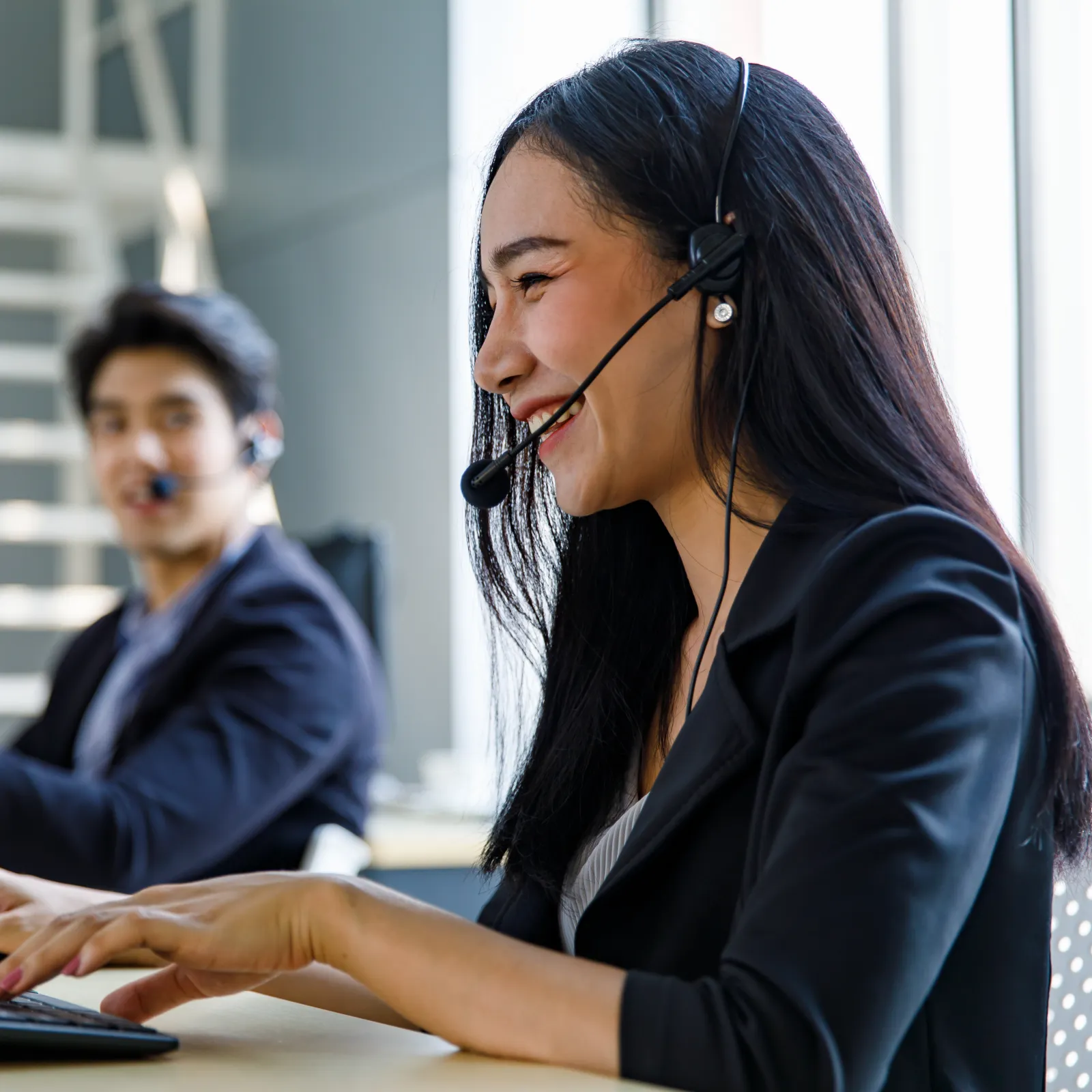 Two customer service representatives wearing headsets working on computers in a modern office environment
