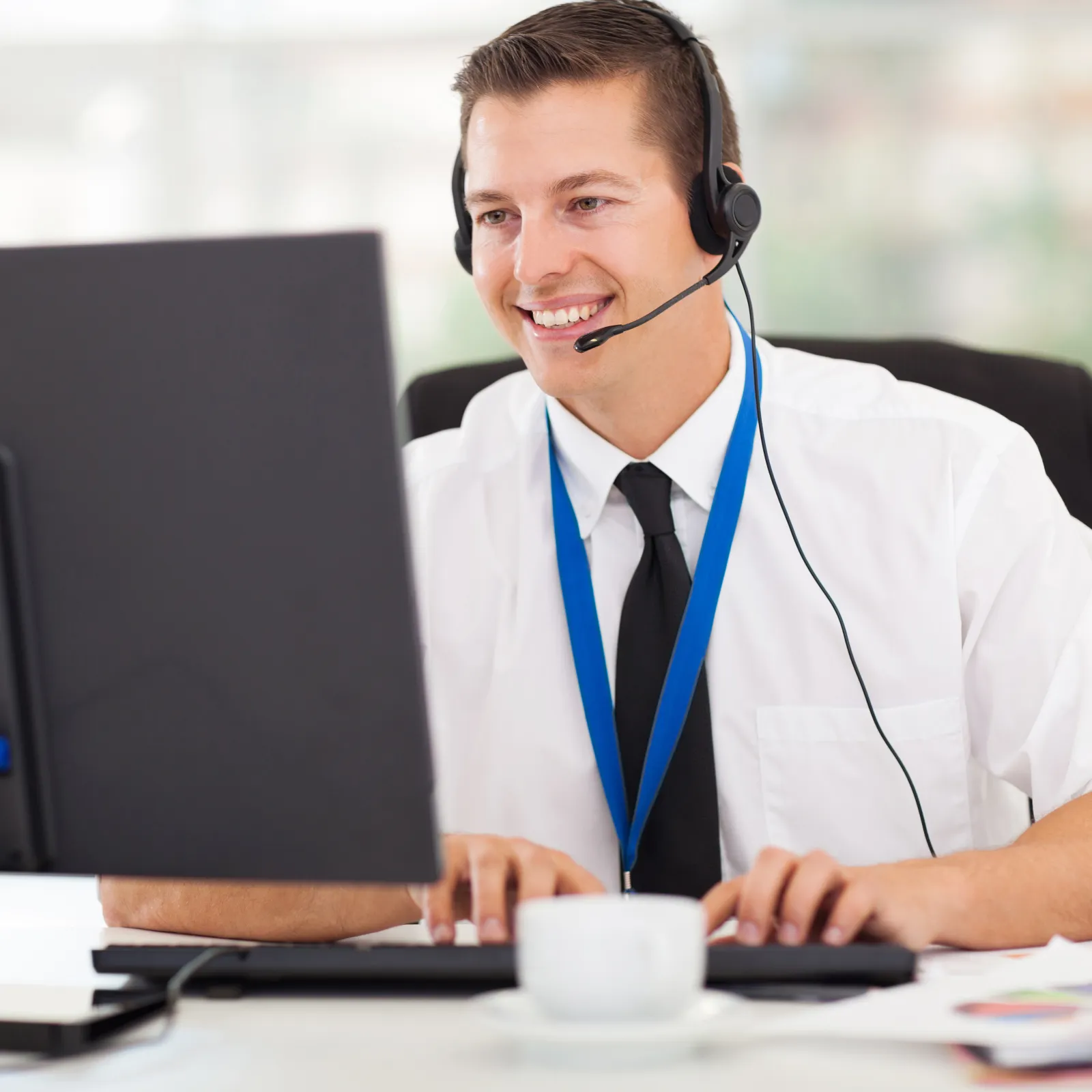 Smiling customer service agent wearing headset and typing on keyboard at office desk with computer