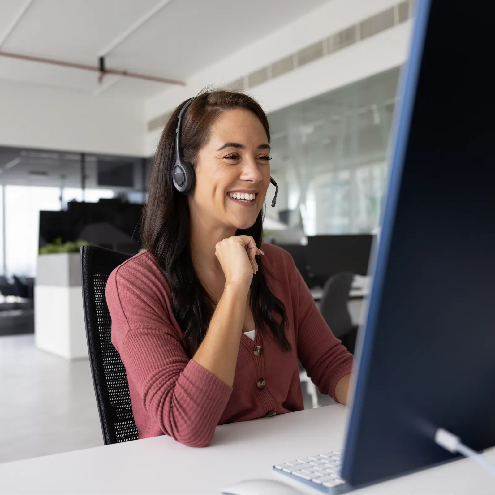 Smiling woman wearing headset working on desktop computer in a modern bright office environment