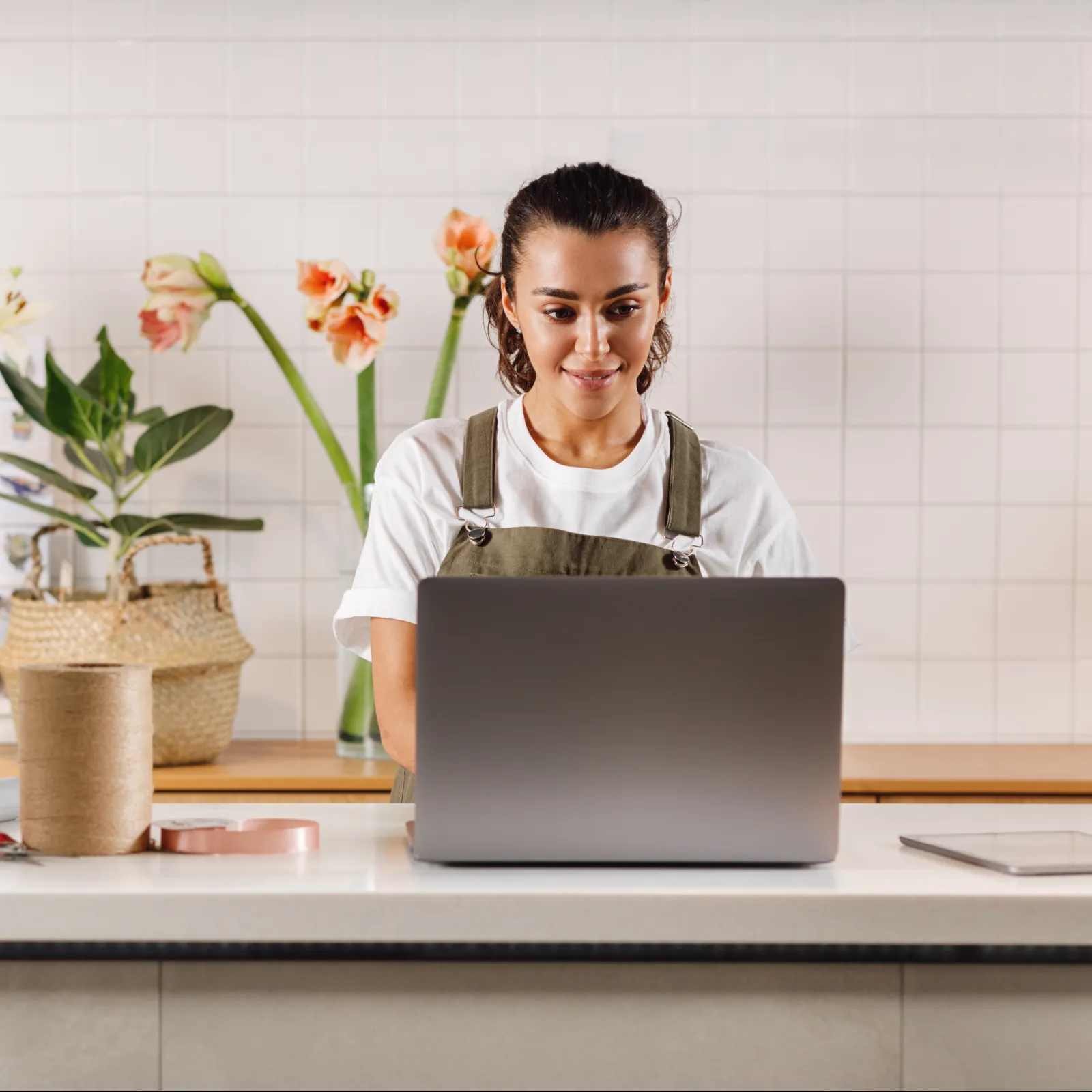 Smiling female scientist in lab coat using a tablet in a bright modern laboratory with colleague working in background