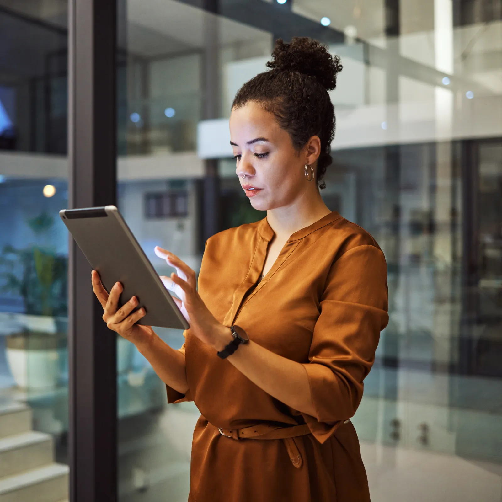 Young professional woman in brown dress using a tablet in a modern office environment at night.