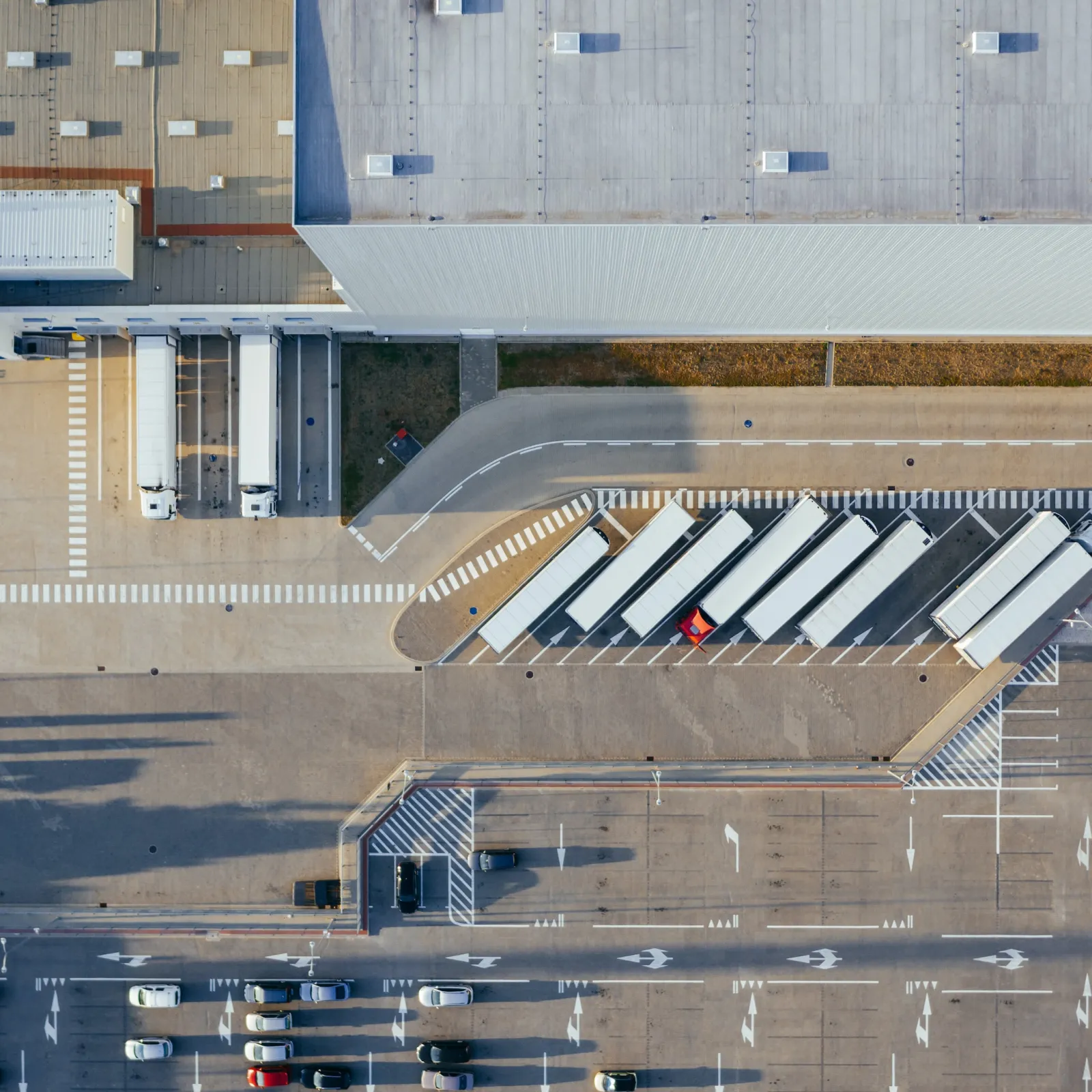 Aerial view of a warehouse with trucks parked in loading bays and cars in the parking lot.