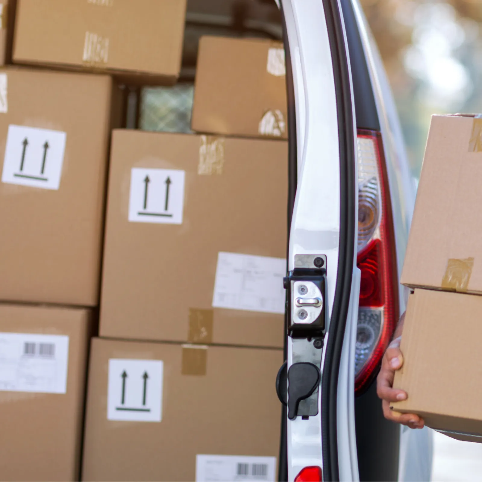 Delivery worker carrying cardboard boxes into van filled with stacked shipping packages outdoors.