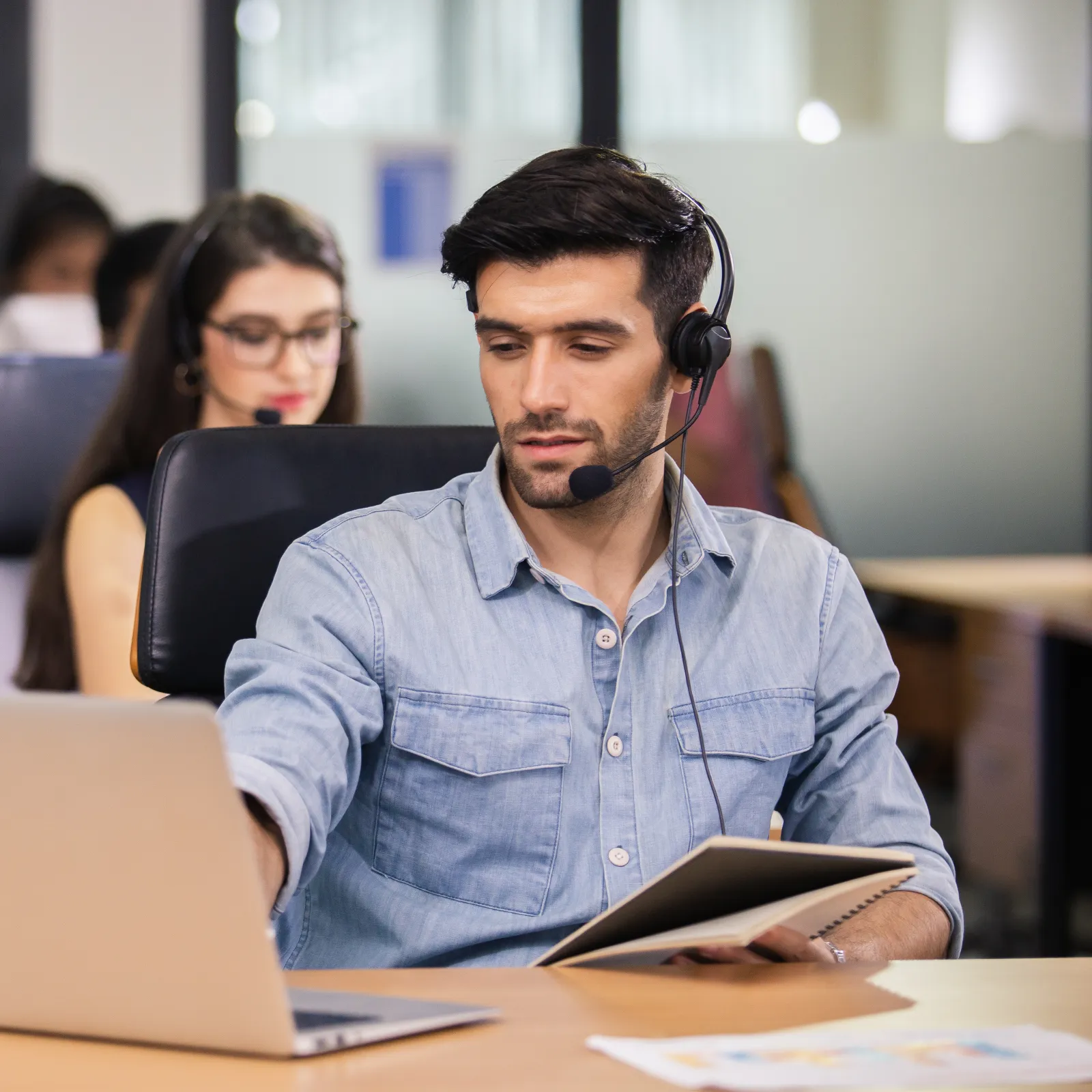 Customer service agents working with headsets in a modern office using laptops and tablets.