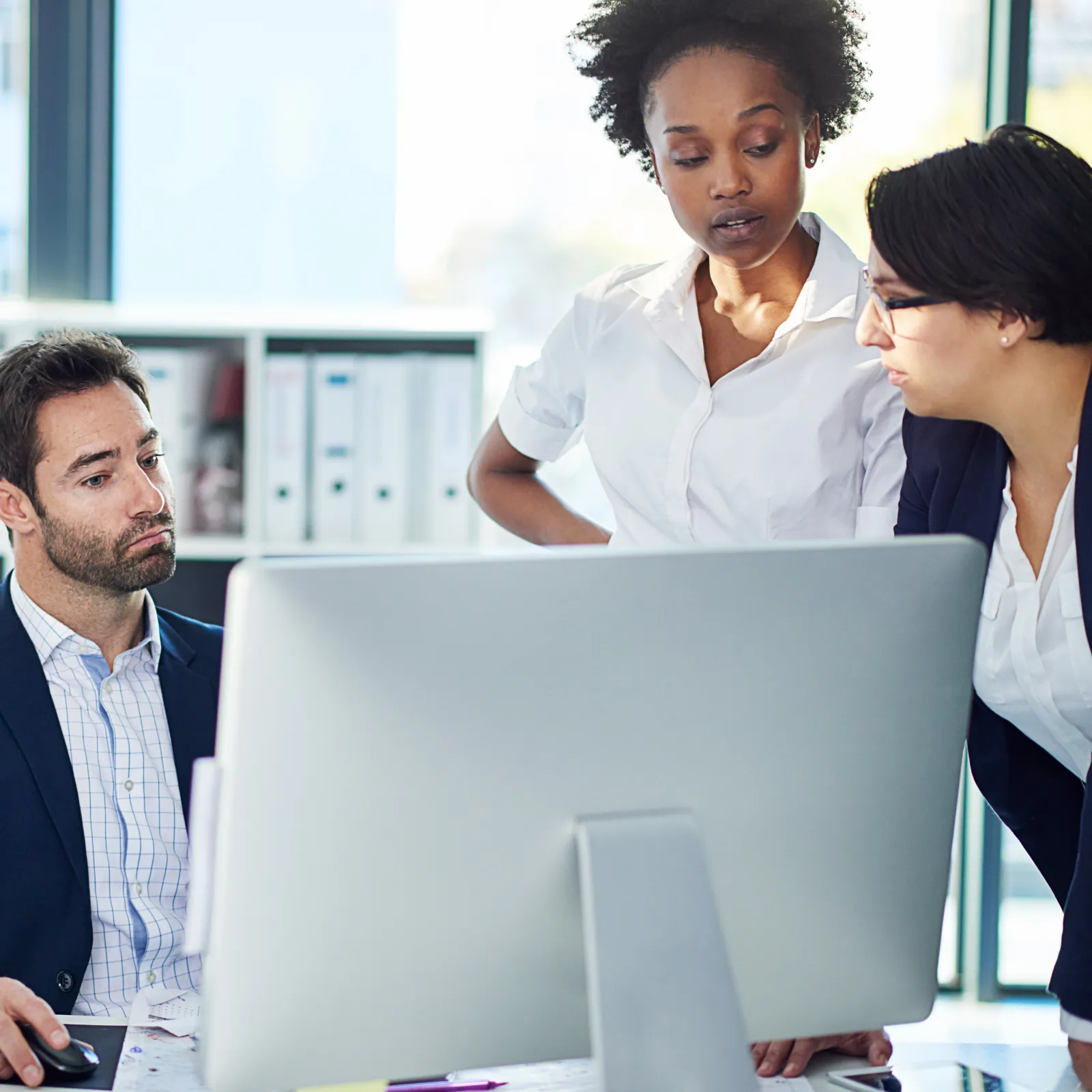 Four diverse professionals collaborating around a computer in a modern office setting during a work meeting.