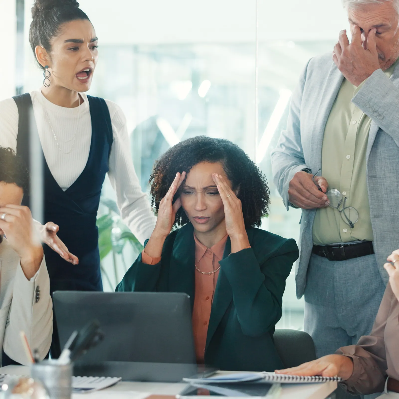 Stressed diverse business team gathered around laptop showing frustration and concern in office meeting.