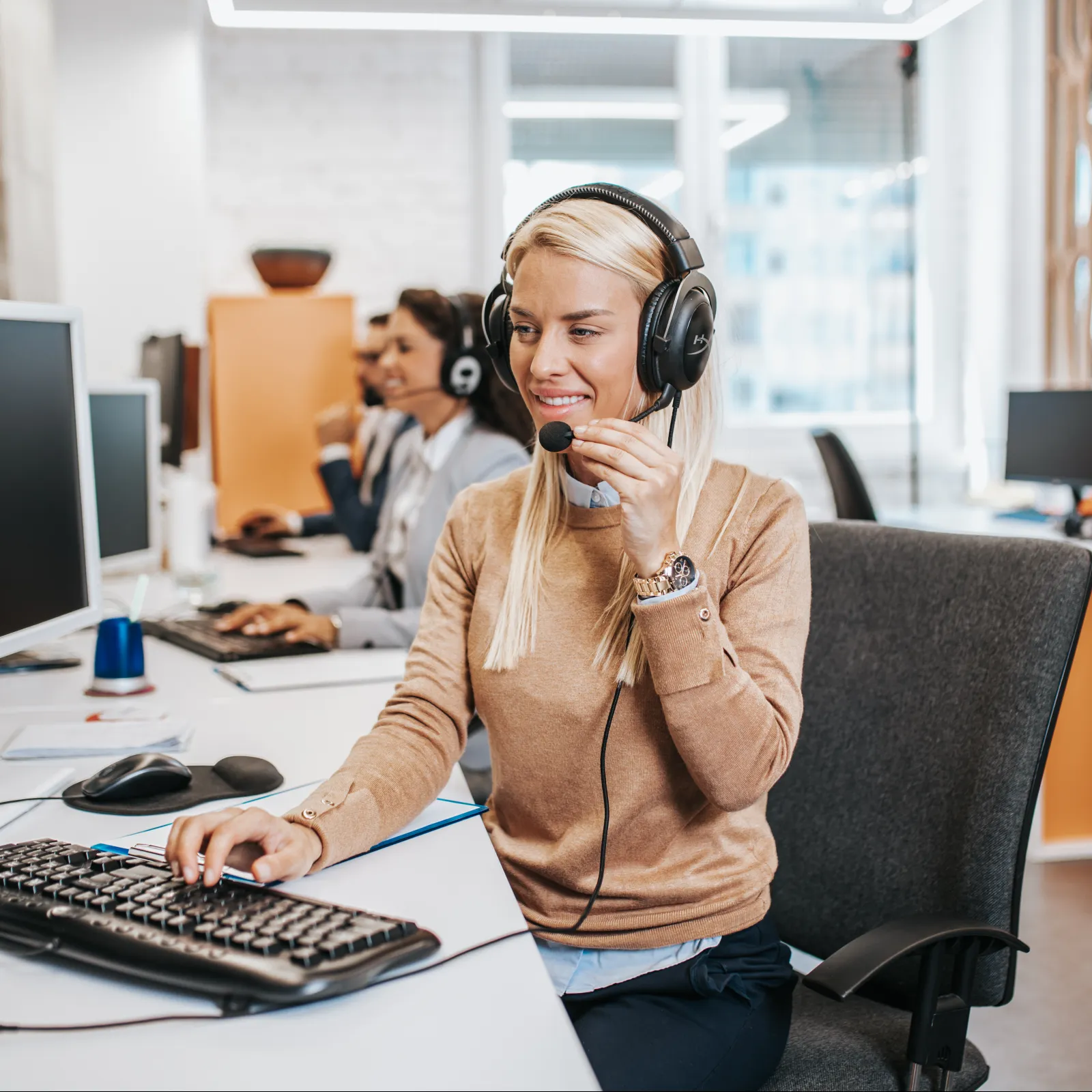 Customer support agents wearing headsets working at computers in a modern office environment.