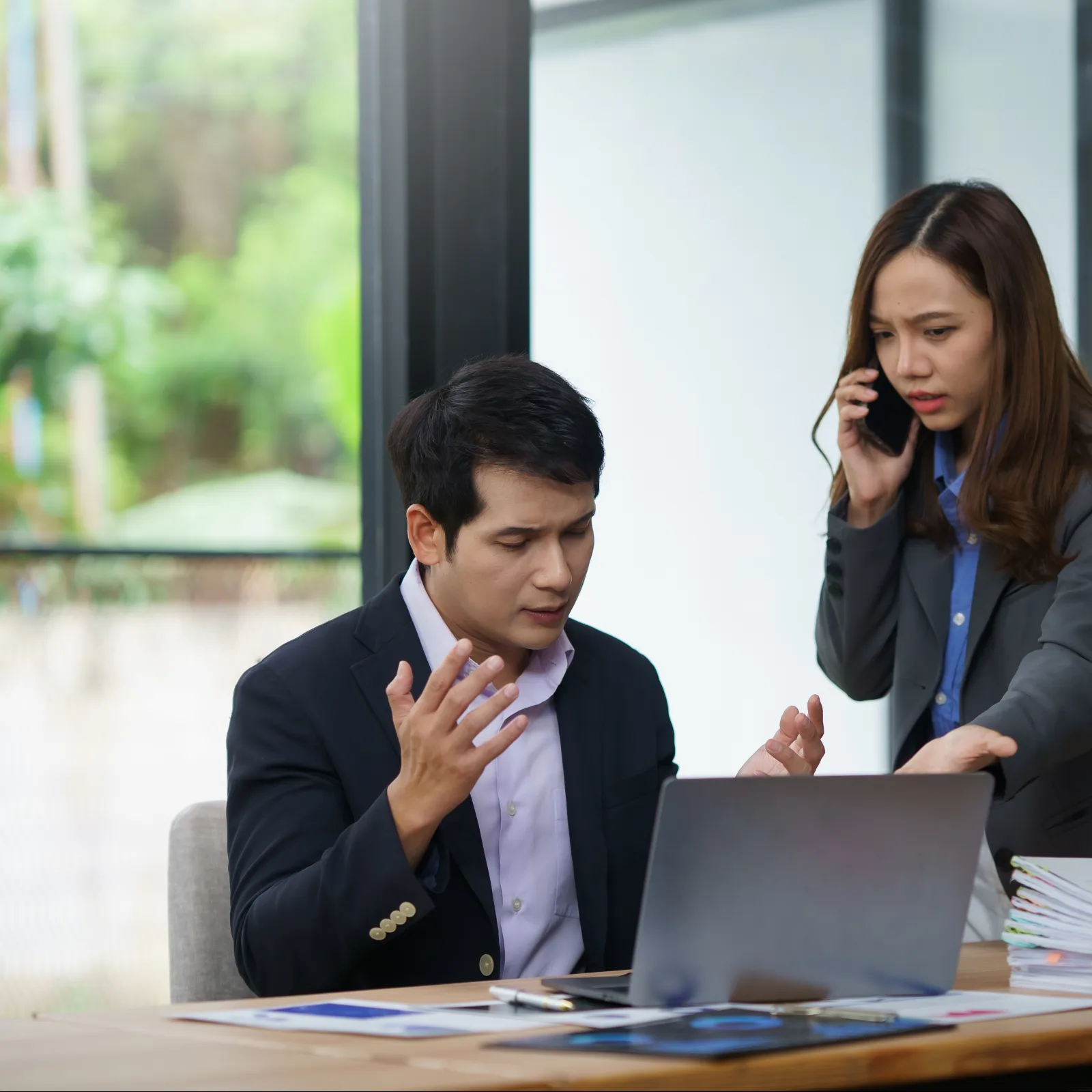 Frustrated business colleagues discussing work issues with laptop and documents in modern office setting.