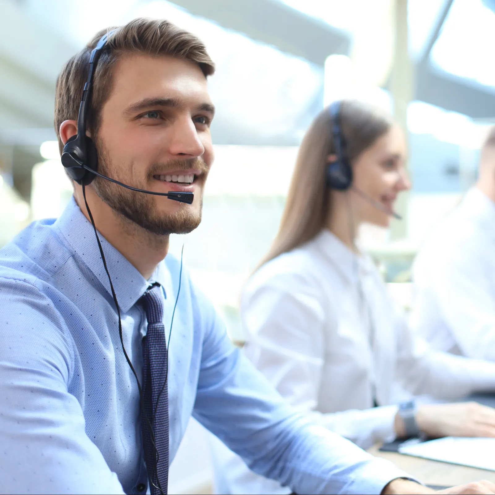 Smiling call center agents wearing headsets working at computers in a bright office environment