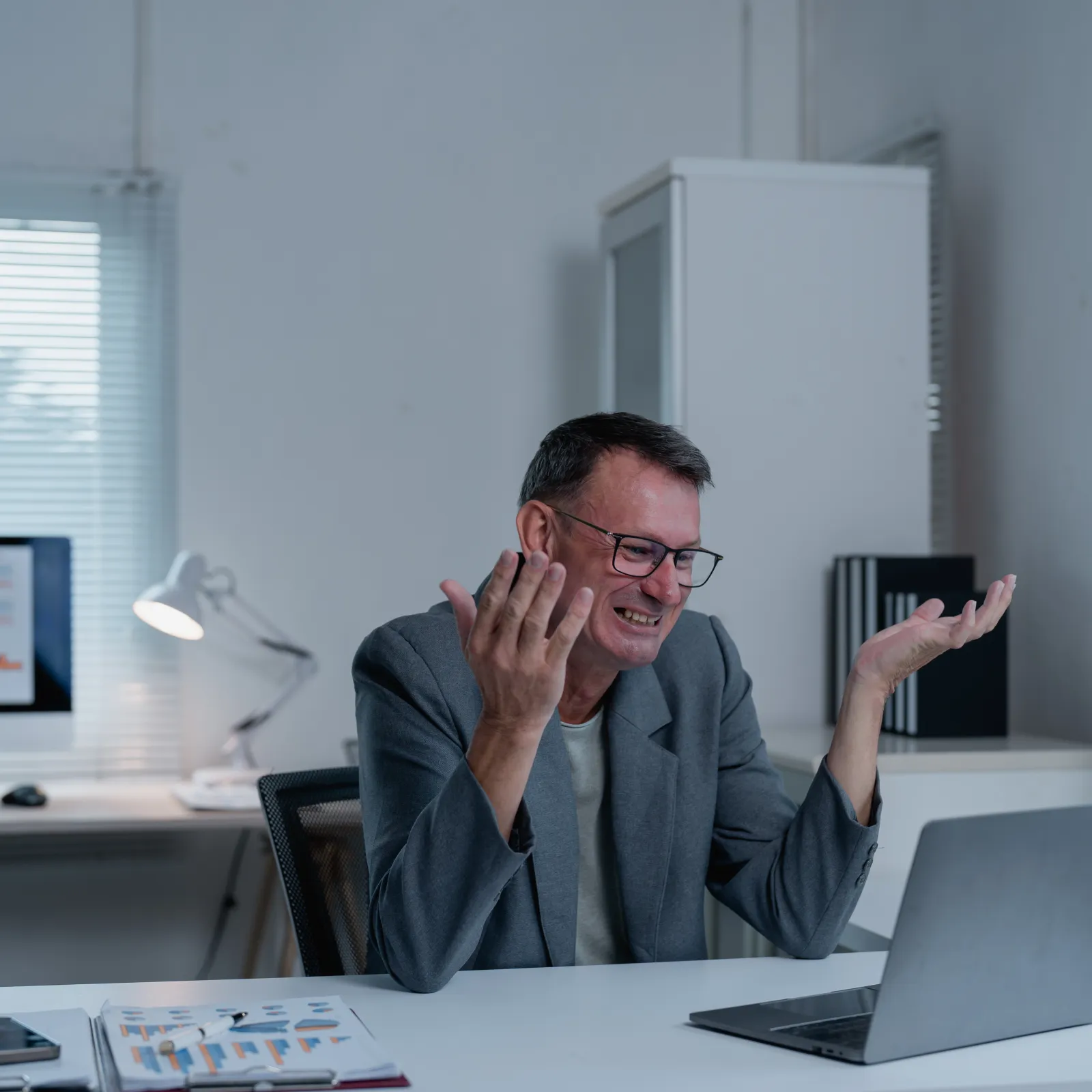 Frustrated businessman reacting to poor laptop results in office with charts on screens behind him