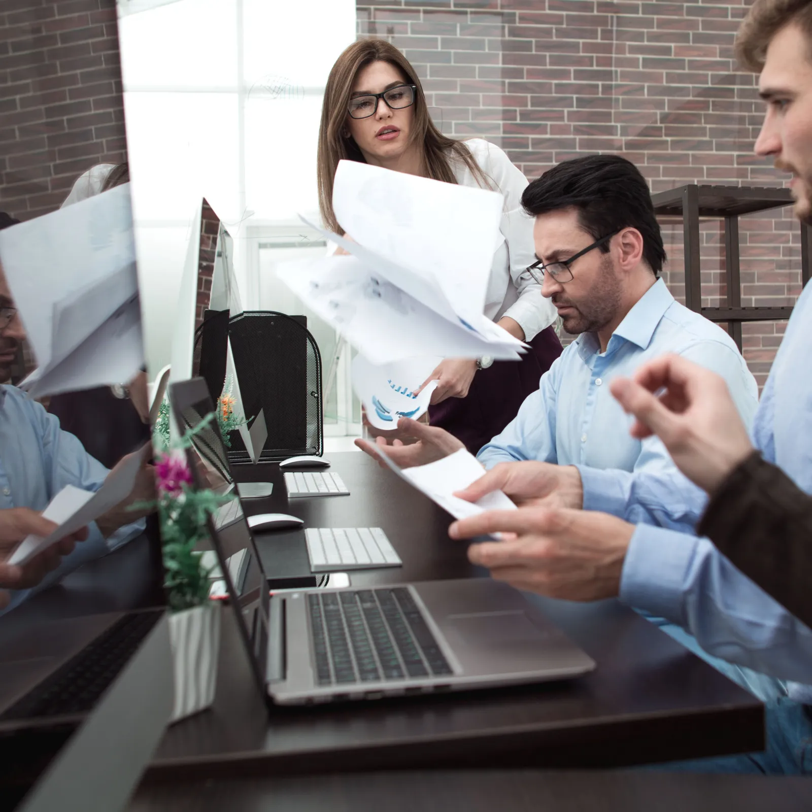 Team of business professionals reviewing documents and working on laptops in modern office setting