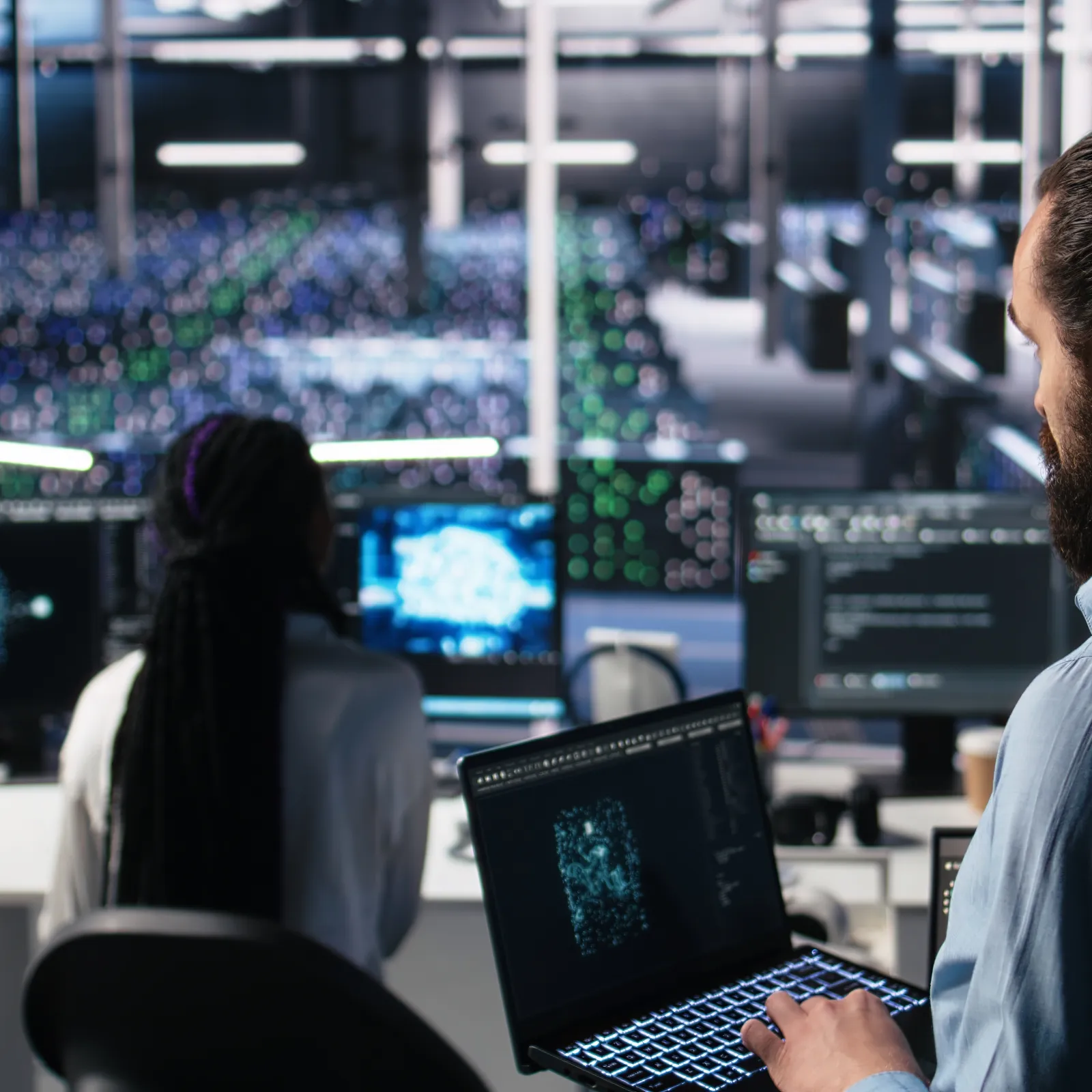 Two IT professionals analyzing complex digital data on multiple screens in a modern high-tech office environment