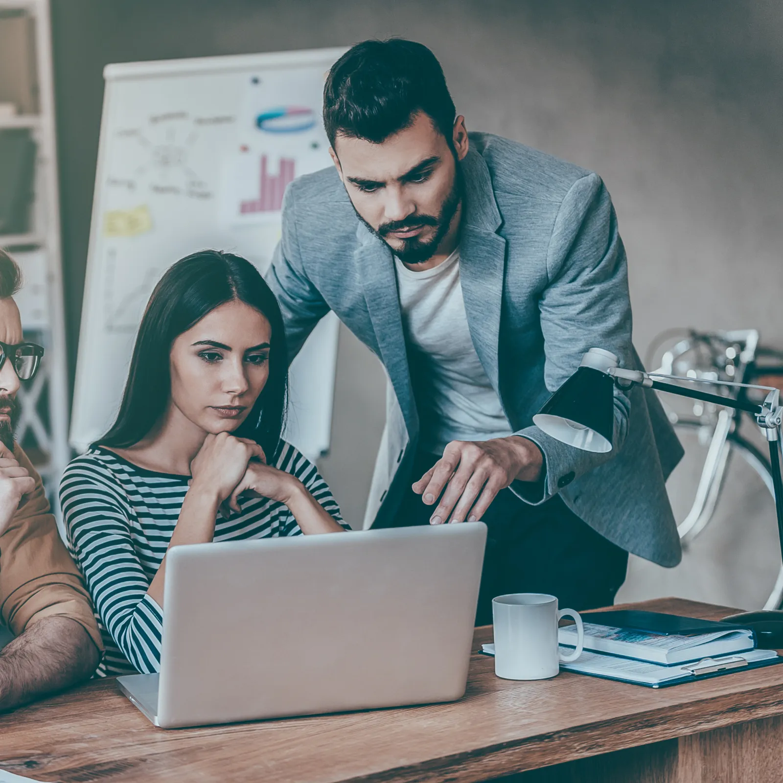 Three professionals focused on a laptop screen in a modern office working collaboratively on a project.