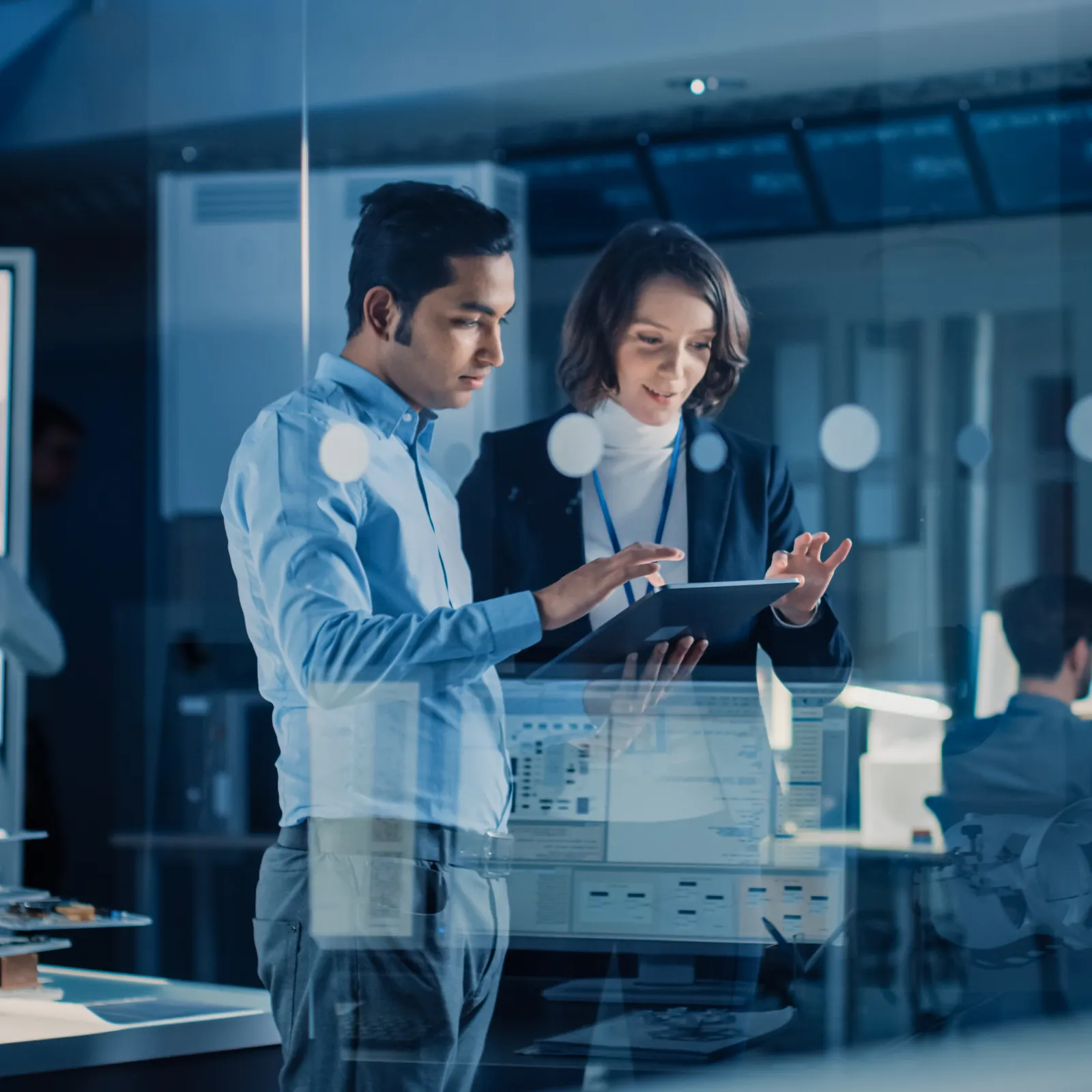 Two engineers discussing project details on a tablet in a modern high-tech office workspace.