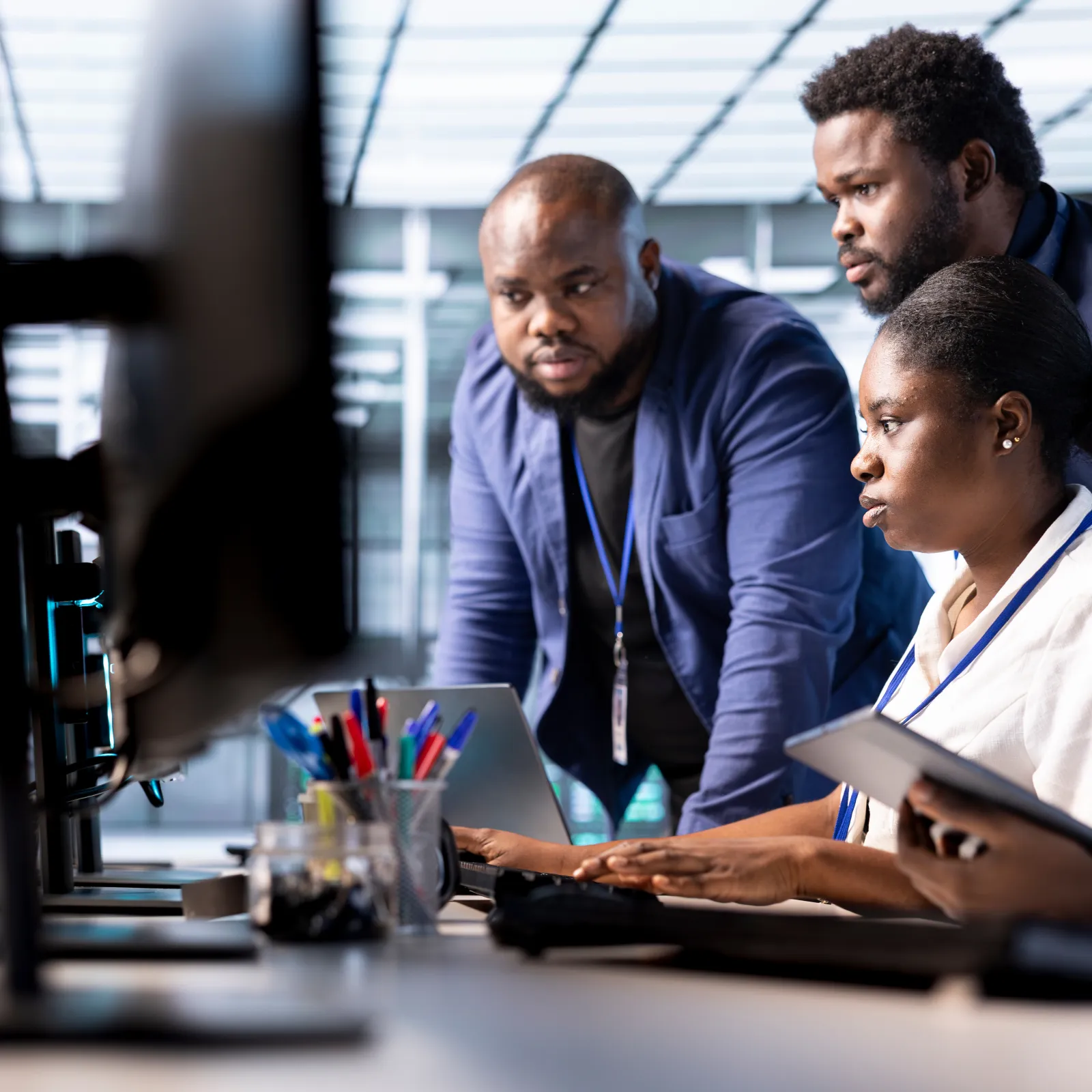 Three professionals collaborate intently at a computer workstation in a modern office setting.