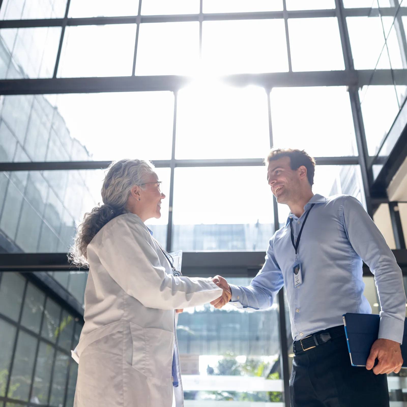 Two professionals shaking hands in a bright modern office lobby with large glass windows.