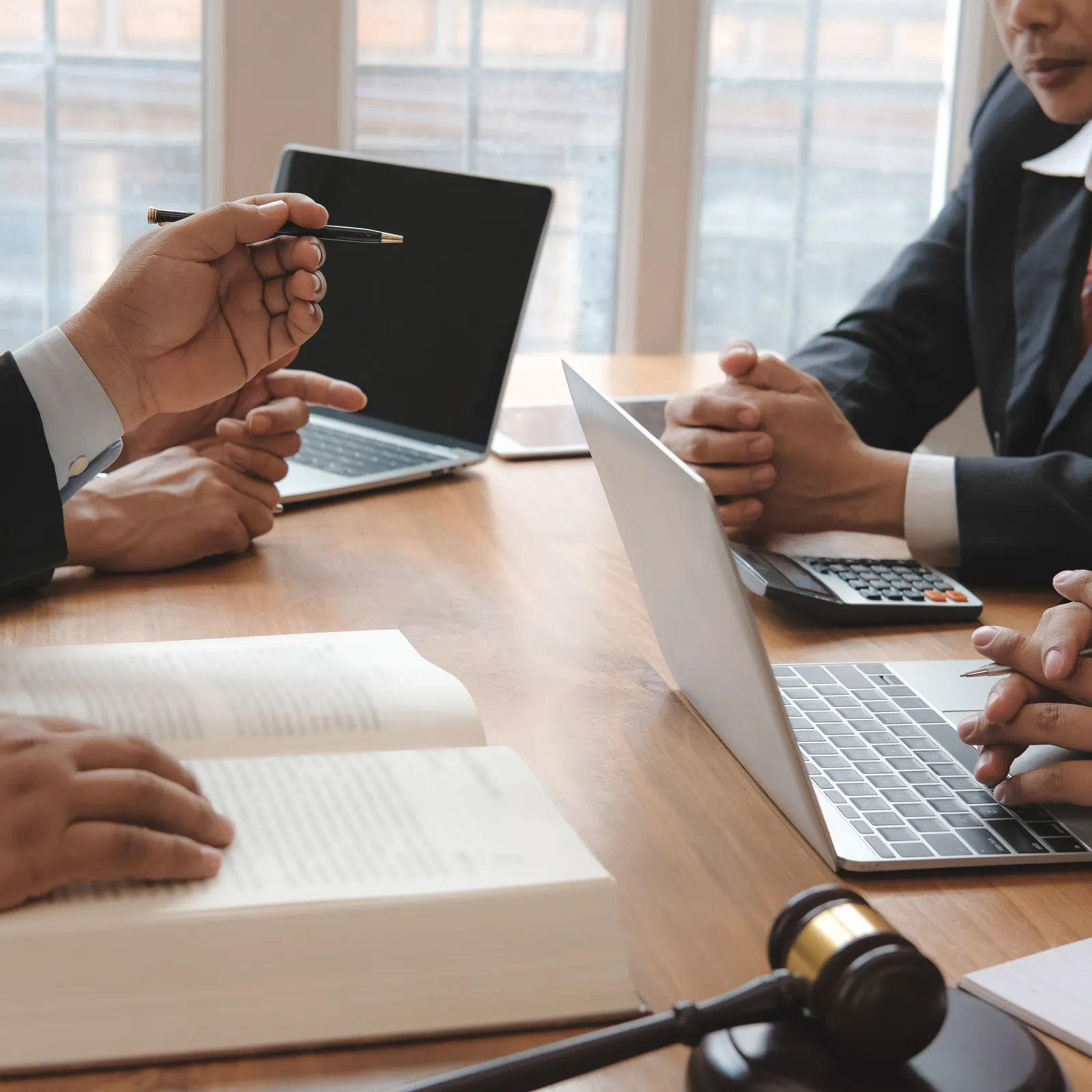 Business professionals discussing legal documents with laptops, book, and gavel on table in office meeting.