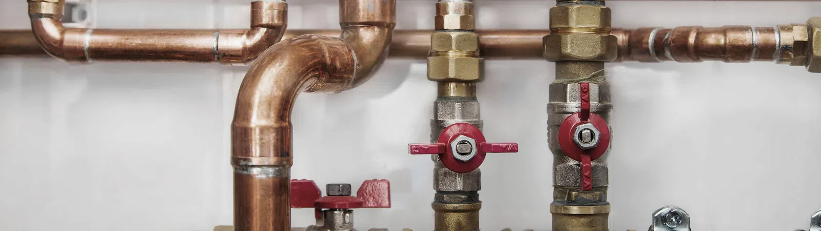 Detailed view of copper plumbing pipes with red valve handles and brass fittings against a white background.