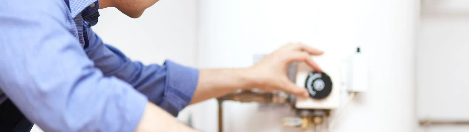 Technician adjusting controls on a white water heater in a utility room wearing a cap and blue shirt.