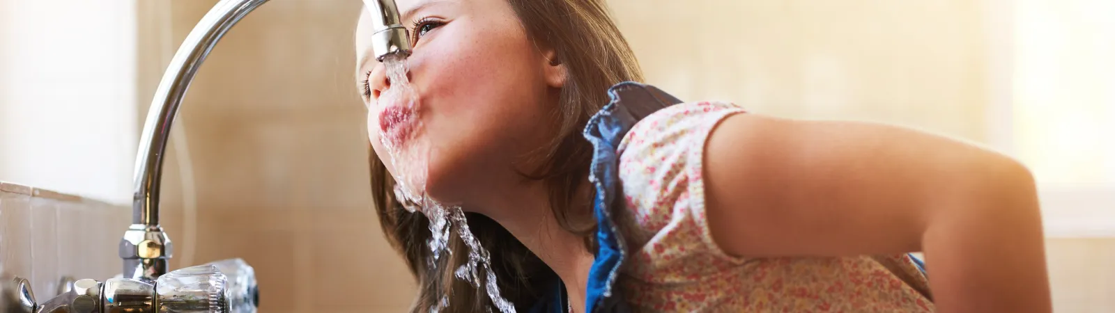 young child drinking water from the faucet