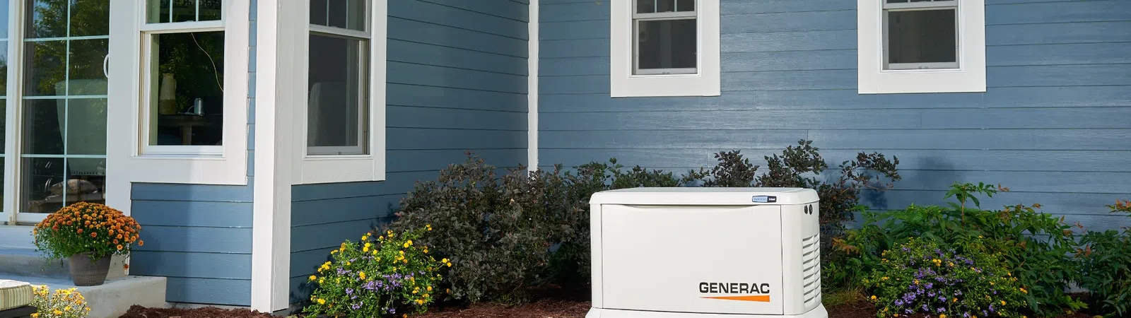 Generac home standby generator installed outside a blue house with landscaping and green grass.