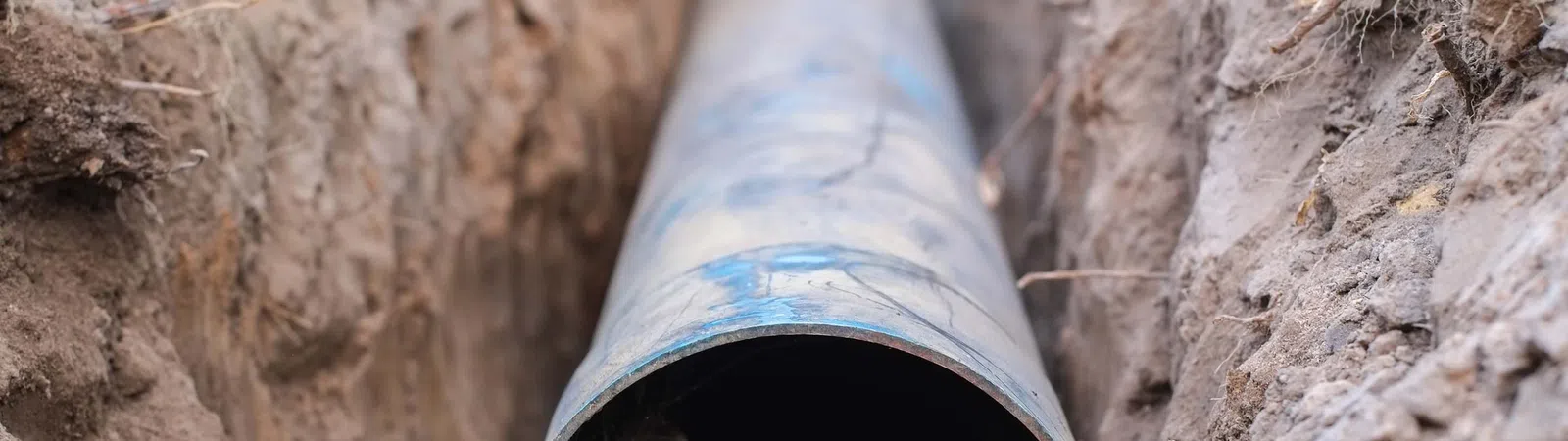 Close-up of a large metal pipe laid in a dirt trench for underground installation or repair work.