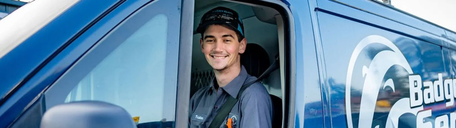 Smiling technician in uniform sitting in blue Badger Bob's Services van with company logo and service list
